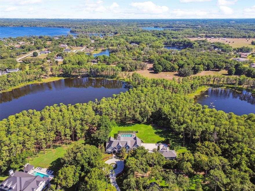 One of Odessa's most exquisite properties comes to market! Perfectly nestled on 3.8 acres between 2 private lakes, this stunning estate offers a 4,400 s.f main house+ a 750 s.f. separate dwelling perfect for in-laws or make it your own creative flexible space! Beauty abounds upon arrival, from the circular driveway with three-tier water fountain to the luxurious lakeside setting. The estate is surrounded by beautiful lush landscaping along the water with acres of yard space perfect for family's seeking privacy and functionality!  The beveled glass front door leads you into an elegant interior, delicately adorned with neutral décor finishes, travertine flooring, crown moldings, wood floors and natural light throughout. A sweeping staircase enhances the grand greeting in the foyer, while just to the right awaits the dining room with decorative columns, designer lighting and a butler’s pantry with a wine chiller. Make your way to the gathering room, complete with a soaring stone fireplace, clerestory windows and built-ins, offering an ideal environment for entertaining. Fit for a chef, the kitchen boasts solid wood cabinetry, a center island, Cambria quartz countertops and high-end appliances that include a Sub-Zero refrigerator, Wolf six-burner gas cooktop, Wolf double oven and warming drawer, as well as two Fisher + Paykel dishwasher drawers. Retreat to the master suite, a secluded escape with double door entry, a spacious walk-in closet and a spa-like bath with dual bath vanities, whirlpool tub with jets and a walk-in shower with double rain heads. Additionally, on the first floor is a private guest suite with a double-door entry, full bath and a walk-in closet. The upstairs offers plenty of room to accommodate guests, from the multipurpose room and flex/loft space to the two bedrooms sharing a Jack-and-Jill bath. An opulent oasis, the exterior space features a sparkling saltwater pool, spa, outdoor shower and a covered patio with a tongue-and-groove ceiling. The gated community of Council Crest has 11 large custom estate homes from 4,400s.f to upwards of 13,000s.f. Quick assess to the Veterans Expy, SR 54 and less than 10 minutes to A+district of Hammond Elementary, Martinez Middle, and Steinbrenner High!
