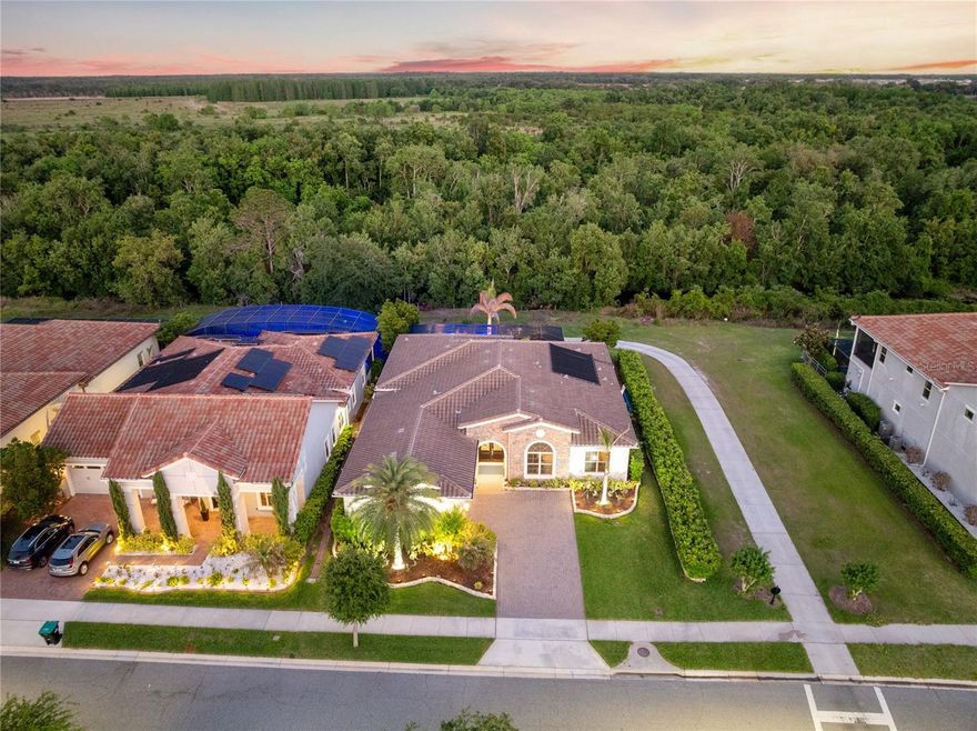 Set within Eagle Creek's guard-gated golf community, this meticulously maintained Spanish Mediterranean residence delivers a level of design and outdoor living that stands apart from every comparable home on the street. With 4 bedrooms, 4 baths, and 3,038 square feet entirely on one floor, the single-story plan is the defining architectural advantage, with every living area, bedroom, and primary space on one seamless level. The home backs to protected conservation and sits across from the Eagle Creek golf course.
The foyer opens with a coffered tray ceiling, designer chandelier, and imported Italian tile niches with gold-trimmed accent lighting. Wide-plank luxury vinyl flooring draws you into the great room, where a full-height Italian tile feature wall anchors the space: blue-veined stone, floor-to-ceiling gold-trimmed display niches, LED lighting, and an electric linear fireplace. The dining room carries the same intention with a custom mirror and wood feature wall. A built-out bar with espresso cabinetry, quartz countertops, and a wine refrigerator serves the entertaining zone just off the living area.
The kitchen is anchored by a quartz island with an apron farmhouse sink, Ann Sacks handmade tile on the island base, gold hardware, espresso cabinetry, subway tile backsplash, chimney hood, gas cooktop, double wall ovens, and a stainless refrigerator. French doors open to a custom appliance pantry with dedicated cabinetry, open shelving, and a one-of-a-kind built-in cabinet. The primary suite enters through a barn door on black track hardware into a charcoal tray ceiling bedroom with an Italian marble fireplace feature wall, dedicated sitting area, and conservation views. The bath is finished floor-to-ceiling in Italian marble tile, with dual vanity, Kohler matte black fixtures, three lighted round mirrors, frameless glass walk-in shower, and a chandelier-lit private water closet. A mirrored door conceals a fully built-out private vanity suite. The walk-in closet features a full custom system with center island.
The covered lanai features a tongue-and-groove cedar ceiling, full outdoor kitchen with stainless grill and chimney hood, Ann Sacks tile backsplash, and a retractable Phantom Screen system. Wide-plank wood decking transitions to travertine pavers at the solar-heated gunite pool with heated spillover spa. A pergola and propane fire pit on a raised wood deck create a third outdoor zone along the conservation hedge. System highlights include whole-house water filtration, EV charging, Lutron smart lighting, and a generator-ready panel. Minutes from Lake Nona Town Center, Medical City, and Orlando International Airport, within Eagle Creek's 24-hour guard-gated golf community.
