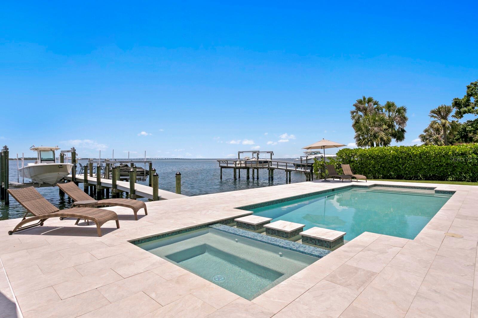 Introducing an exquisite blend of sophisticated coastal living and wide-open bay views in this 2020-built Sunset Park waterfront estate, thoughtfully enhanced with over half a million dollars in curated upgrades. From the moment you step through the stylish double doors, you're drawn in by breathtaking open-water views, framed by a warm, neutral palette and rich hardwood floors, adding the perfect finishing touch. Built to the highest standards with concrete block construction, impact-rated windows and doors, every detail of this home has been thoughtfully curated for style, function, and resilience. The first level offers a seamless layout for entertaining, featuring a formal living room with fireplace, a formal dining room, and an inviting family room anchored by a media feature wall. The chef’s kitchen is designed for both intimate and large-scale gatherings, boasting honed marble countertops, a generous center island, Wolf and Sub-Zero appliances, a large butler’s pantry, and wine refrigeration. An ensuite guest suite and a stylish powder bath complete the first floor. Upstairs, enjoy a spacious loft and five ensuite bedrooms (or Optional Bonus Room), including a luxurious primary suite offering panoramic bay views, a sitting area, an oversized custom closet/dressing room, and a private terrace overlooking the water. The marble-clad primary bath is a sanctuary featuring a soaking tub, a glass-enclosed shower, and a morning bar with a beverage station. Retracting glass doors lead to a spacious covered waterfront terrace with a fully equipped outdoor kitchen—perfect for seamless indoor-outdoor entertainment. The backyard has been extensively upgraded with a pool and spa, as well as a reimagined patio surrounded by professionally designed landscaping and ambient uplighting. Enjoy 90 feet of deep-water frontage with a new dock and dual boat/jet ski lifts (16,000 and 10,000 lbs), ideal for boating enthusiasts. A Control4 smart home automation and a full-home surround sound system elevate comfort and connectivity throughout. Additional thoughtful upgrades include automated window treatments, custom blinds, updated lighting and ceiling fans, garage cabinetry, a water softener system, and a 3+ car garage with room for lifts, which completes the offering. This elevated home remained high and dry during inclement weather. All just minutes from top-rated schools, Downtown Tampa, International Plaza, Tampa International Airport, and the Gulf Coast’s best beaches—this is the ultimate in refined waterfront living. Available furnished at additional cost.