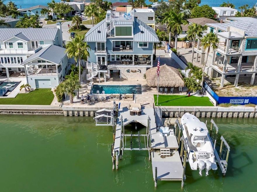 Under contract-accepting backup offers. 85ft OF WATER FRONTAGE | 2 BOAT LIFTS | 2 JETSKI LIFTS | PANORAMIC WATERVIEWS | PRIVATE ELEVATOR. Welcome to the most remarkable waterfront residences on St. Pete Beach, where coastal living, craftsmanship, and pure relaxation unite. The ultimate outdoor experience while maintaining peace of mind with full elevation, impact-rated windows and doors, and an outdoor oasis that surpasses every expectation. Step onto your own PRIVATE MARINA with an expansive composite dock featuring two boat lifts (30K and 10K), dual jet ski lifts, water, electric, newer seawall, and a fish-cleaning station for your fresh catch. Located on the Intracoastal waterway with quick Gulf access this is a fisherman/boater's dream. The backyard transforms into a resort-style escape with a SALTWATER PEBBLE TECH POOL featuring three cascading waterfalls, in-water seating, a sun shelf, and a heater/chiller system for ideal comfort in every season. Surrounding it all is elegant Travertine tile connecting multiple entertaining areas, a massive authentic TIKI HUT (22' x 24'), and low-maintenance artificial turf ensures your time is spent relaxing, not mowing. Step through the custom front door and enter into 3,489 square feet of luxurious living space (4,856 Total Gross Area) where an abundance of light fills every room, high ceilings and uninterrupted water vistas through floor-to-ceiling hurricane-rated frameless windows. The open-concept great room boasts a custom bar accented with wood trim and complete with its own refrigerator and sink. Designed for the modern chef, the custom kitchen boasts stainless-steel cabinetry, Quartz counters, four THOR refrigerator drawers, and premium stainless-steel appliances throughout. A dining area, half bath, and a butler’s pantry/utility room complete this level. The second-level covered porch overlooks the INTRACOASTAL and is complete with tongue and groove wood ceilings, tile floors, ceiling fans, electric shades, and a built-in propane gas connection for your grill. Enjoy Sonos-powered music throughout every level, inside and out. The third floor offers a split-bedroom layout with a cozy entertainment lounge and fireplace with sliders leading the third level covered balcony. Two guest bedrooms share a well-appointed bath, while the primary suite enjoys dual closets, a gas fireplace, and a private balcony. It's SPA-INSPIRED bathroom completes the retreat with sophistication and serenity. The fourth floor presents a versatile guest suite with its own bath, an all-glass sitting area, plus direct access to the ROOFTOP DECK which is the highest residential vantage point in St. Pete Beach. From here, take in 360-degree panoramas of downtown St. Petersburg, Tropicana Field, the Don CeSar, Boca Ciega Bay, and the Gulf. This deck is the ultimate perch for sunrise coffees, sunset toasts, and dolphin watching. The ground floor has a two-car garage, dual storage rooms, a bar area with roll-up door to the pool, a bonus recreation room, and a full bath. The oversized paver driveway offers ample space to accommodate multiple vehicles with ease. The entire exterior was reimagined with maintenance free Hardie Plank siding, new eaves, PVC fascia, gutters, and lifetime metal roof (2025), all designed for durability and style. Every surface of this home has been thoughtfully upgraded with precision and purpose. This is not just another waterfront home, it’s a custom-crafted sanctuary designed for those who want to live every day like a vacation.