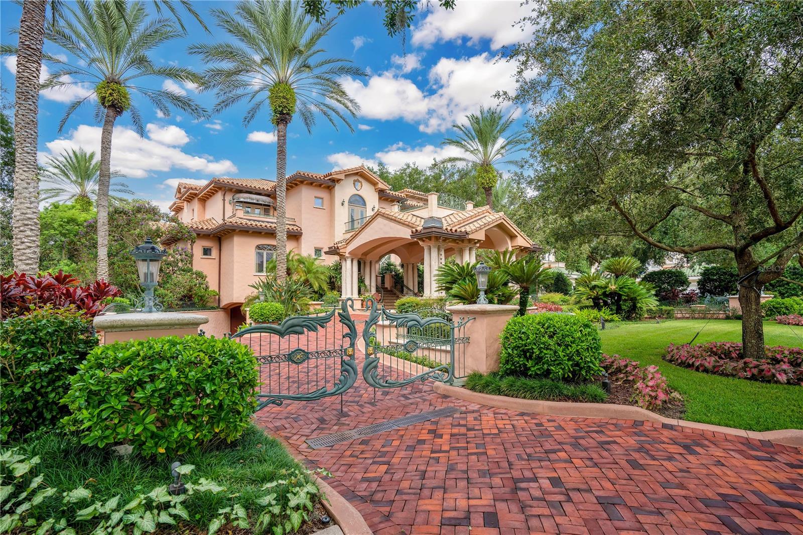 Nestled on the shores of Lake Butler, Puesta del Sol is a masterpiece of design and luxury, just a short walk from the renowned Isleworth Golf & Country Club. Named for the breathtaking sunsets visible from its many terraces, this estate was crafted for grand entertaining and elegant living.
From the bold elegance of the grand porte-cochère entry to the graceful curves of its architectural design, every detail reflects sophistication. Rich finishes of granite, Botticino marble, stone, and iron create a timeless aesthetic, while soaring 26-foot ceilings in the living room highlight the stunning coquina and limestone fireplace. The family room is a refined retreat, complete with a custom bar and fireplace.
The art deco-inspired primary suite offers a private terrace and a balcony overlooking the living room, creating a serene sanctuary. Meanwhile, the Orchid Room, adorned with intricate depictions of exotic species, opens to a 750-square-foot pool, featuring a “Rainbow” Bridge and swim-up bar. Adjacent, a private steam room and sauna provide ultimate relaxation.
An enchanting wine cellar, secured by custom iron gates and dramatic torchieres, accommodates 1,500 bottles—a connoisseur’s dream. The convenience of an elevator seamlessly connects the kitchen to the 7,800-square-foot air-conditioned underground garage, ensuring effortless living.
Beyond, a double-gated entry leads to the boathouse, offering direct access to the Butler Chain of Lakes—13 interconnected lakes where natural Florida beauty meets the magic of nightly fireworks.
For those who seek the very best, Puesta del Sol is an unparalleled opportunity to own a true architectural gem. Discover this breathtaking estate and make it your own.