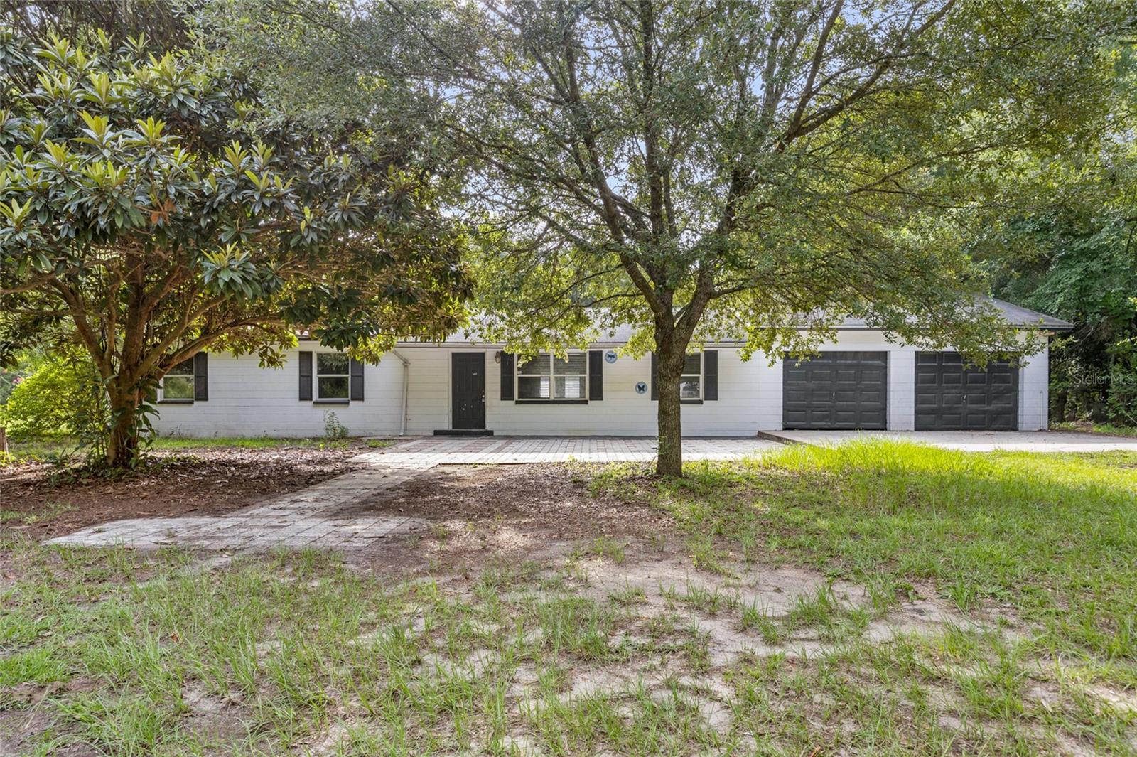 Built to last, this 3-bed, 2-bath concrete block home sits on 2 fully fenced, park-like acres, just minutes from Alachua’s historic downtown! This solidly built residence features an open floor plan, Brazilian wood floors, and renovated island kitchen, complemented by a two-car garage with dedicated workshop. As you approach, a large paver patio welcomes you, while the home itself is nestled among mature trees on property defined by its natural beauty. Stepping indoors you will discover a spacious living room which opens to the dining area and kitchen, showcasing stainless steel appliances including a new dishwasher, granite countertops, wood cabinets, and convenient island. Off the dining area are garden doors leading to the back patio, and a huge laundry room with washer and dryer, and plenty of room for an extra refrigerator, storage, or walk-in pantry. Heading down the hallway you will find an updated guest bath with tub/shower combo, 2 guest bedrooms, and primary suite with updated ensuite bath featuring a walk-in shower with décor tile. Out back is a paver patio that overlooks the tranquil surroundings, making it a relaxing spot to soak up the Florida sunshine. With 2 fenced acres, there is plenty of space for letting little ones run and play, gardening, parking boats and RVs, and enjoying an array of outdoor activities. Ideally situated, the home is in close proximity to the 441 and I-75, 2 miles to Alachua, 9 miles to High Springs, and 19 miles to Gainesville. Cedar Key on the Gulf is a little over an hour away, and the Atlantic beaches are about a 2-hour drive. If you are tired of the hustle and bustle, but want to be close to amenities, you will want to explore this scenic retreat before it is gone!
