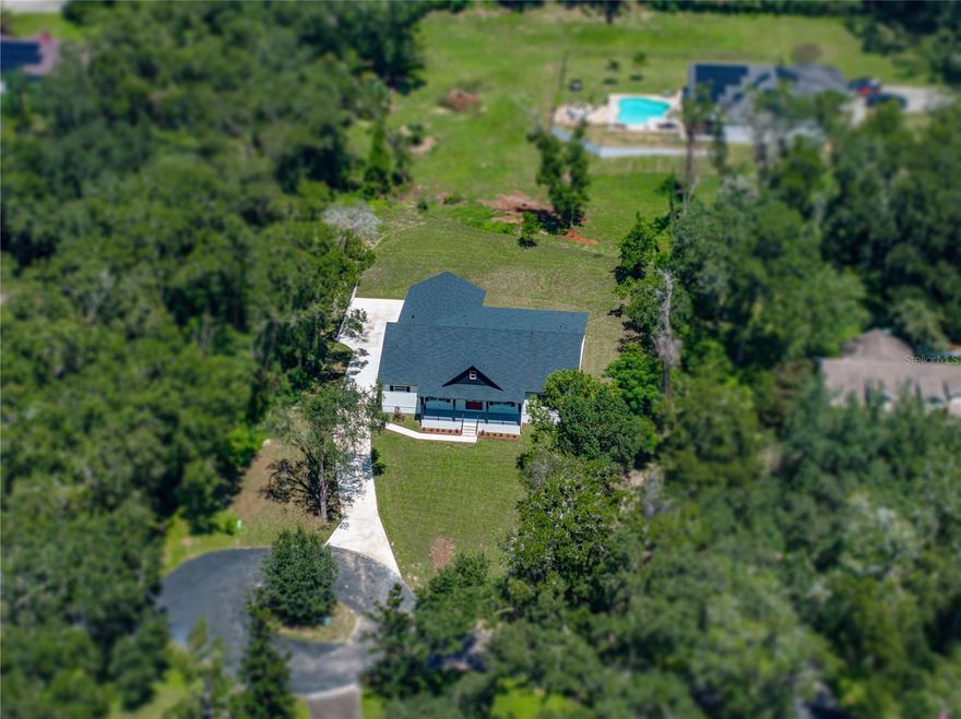 A fresh life of luxury begins in this remarkable 3,197 sq ft custom home built in 2025, perfectly
placed at the end of a cul-de-sac within an intimate eight-home community. Sitting on just over
an acre, close to all that Dade City has to offer, this 5 bedroom, 4 bath, 3 car garage property
delivers a thoughtful layout, high-end finishes, and plenty of space indoors and out with 4,667 sq
ft under roof. A charming front porch greets you with classic board-and-batten accents, modern
colors, and just the right touch of farmhouse character. Inside, soaring vaulted ceilings with
warm wood beams immediately draw the eye upward, setting the tone for the expansive open
layout. Luxury wood-look vinyl plank floors run seamlessly throughout much of the home,
connecting the living room, dining area, and chef’s kitchen into one flowing, light-filled space.
Large sliding glass doors open to a generous covered back porch, extending your living space
outdoors for easy entertaining or quiet evenings. The kitchen was designed for beauty, function,
and entertainment, featuring striking two-toned cabinetry with matte black hardware, a built-in
double oven and microwave, a cooktop, a stainless steel dishwasher, and a refrigerator. A
massive center island offers breakfast bar seating, while glass-faced upper cabinets and a
spacious walk-in butler’s pantry provide abundant storage and display space. Privately tucked
near the front of the home, the first of two suite-style bedrooms offers a one-of-a-kind retreat. Its
spa-inspired bathroom includes a dual-entry walk-through shower, a freestanding soaking tub,
two separate vanities, and a large custom-organized walk-in closet. Down the hall are a full guest
bath, a guest bedroom or office, and a well-appointed laundry room. On the opposite side of the
home, a third bedroom with its own private ensuite and walk-in closet offers plenty of privacy,
while two additional bedrooms share a beautifully designed Jack and Jill bath with dual sinks
and a walk-in shower. The oversized three-car garage is ideal for car enthusiasts or anyone who
values extra space. Every detail in this home
was carefully chosen to create a truly fresh start for its very first owner. Contact us today to
arrange your private showing and experience this exceptional property for yourself.