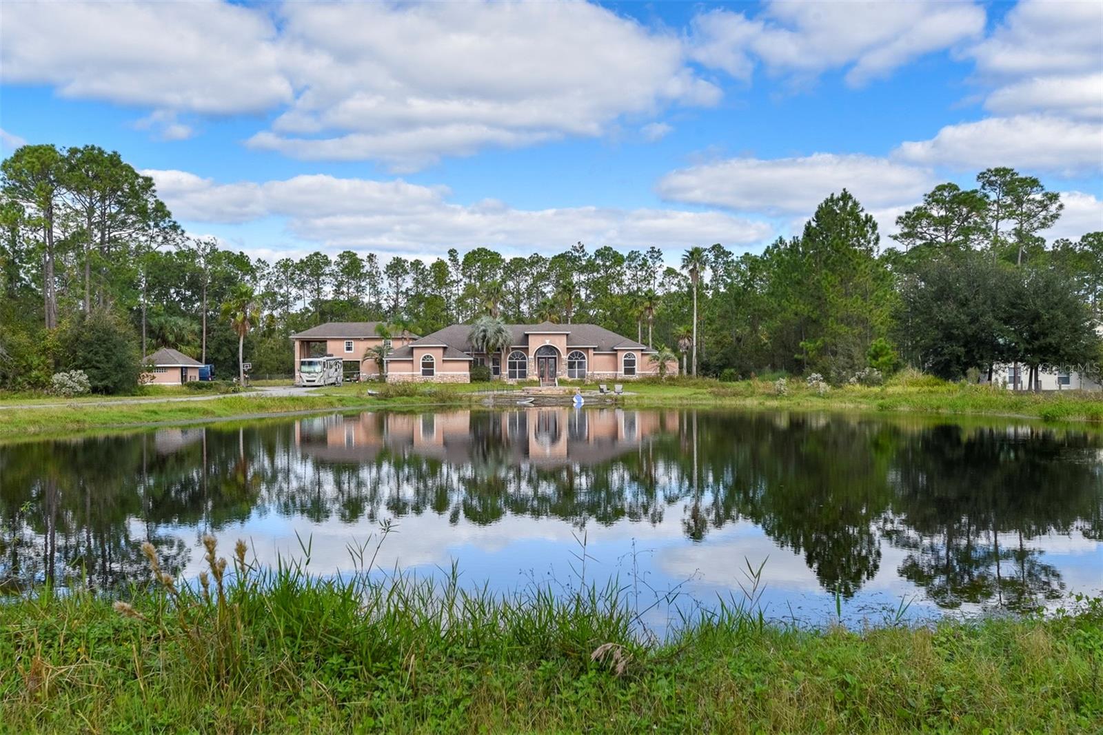 Welcome to your serene 4.5-acre gated country estate, a true sanctuary nestled in a tranquil setting, just 20 minutes from the vibrant Ormond Beach. As you approach, a long private driveway winds gracefully around a picturesque spring-fed pond, culminating at a fountain that welcomes you to this stunning residence. Step inside the expansive 2,800-square-foot split-plan home, where an abundance of natural light fills the living space, creating an inviting atmosphere. Enjoy breathtaking views of the outdoor tropical resort-style swimming pool, complete with a soothing jacuzzi, a dramatic waterfall, beach entry, and a thrilling waterslide crafted from beautifully designed rock formations. To the left lies a chef's dream kitchen, featuring granite countertops, wood cabinets and a cozy sitting bar for casual gatherings. The kitchen flows seamlessly into the formal living room, which boasts a warm fireplace and continues the theme of stunning pool views, making it a perfect spot for entertaining or relaxing with loved ones. The large master bedroom and bathroom include a whirlpool tub overlooking the rock waterfalls, private shower and water closet. Additional features of this exceptional property include soaring high ceilings, a large laundry room complete with a sink, and ample parking for guests. A detached storage unit provides the perfect space for parking ATVs and outdoor equipment. For added flexibility, the property includes a separate one-bedroom, two-bath apartment or in-law suite, complete with its own kitchen and a balcony overlooking the serene grounds—perfect for guests or extended family. Combined with the main home, this brings the total to 4 bedrooms and 4 bathrooms, offering nearly 4,000 sq ft of living space across both structures. Below the apartment, covered RV parking with a 50W amp and a two-car garage provide convenience for all your recreational needs. Conveniently located at the end of a cul-de-sac street with privacy easements on the west and north sides, this property captures the essence of peaceful country living while offering an array of storage options and expansive living space. With its picturesque surroundings and abundant potential, this country estate is ready for the right person to bring it to life with love and care. Don’t miss this opportunity to create your dream retreat!
