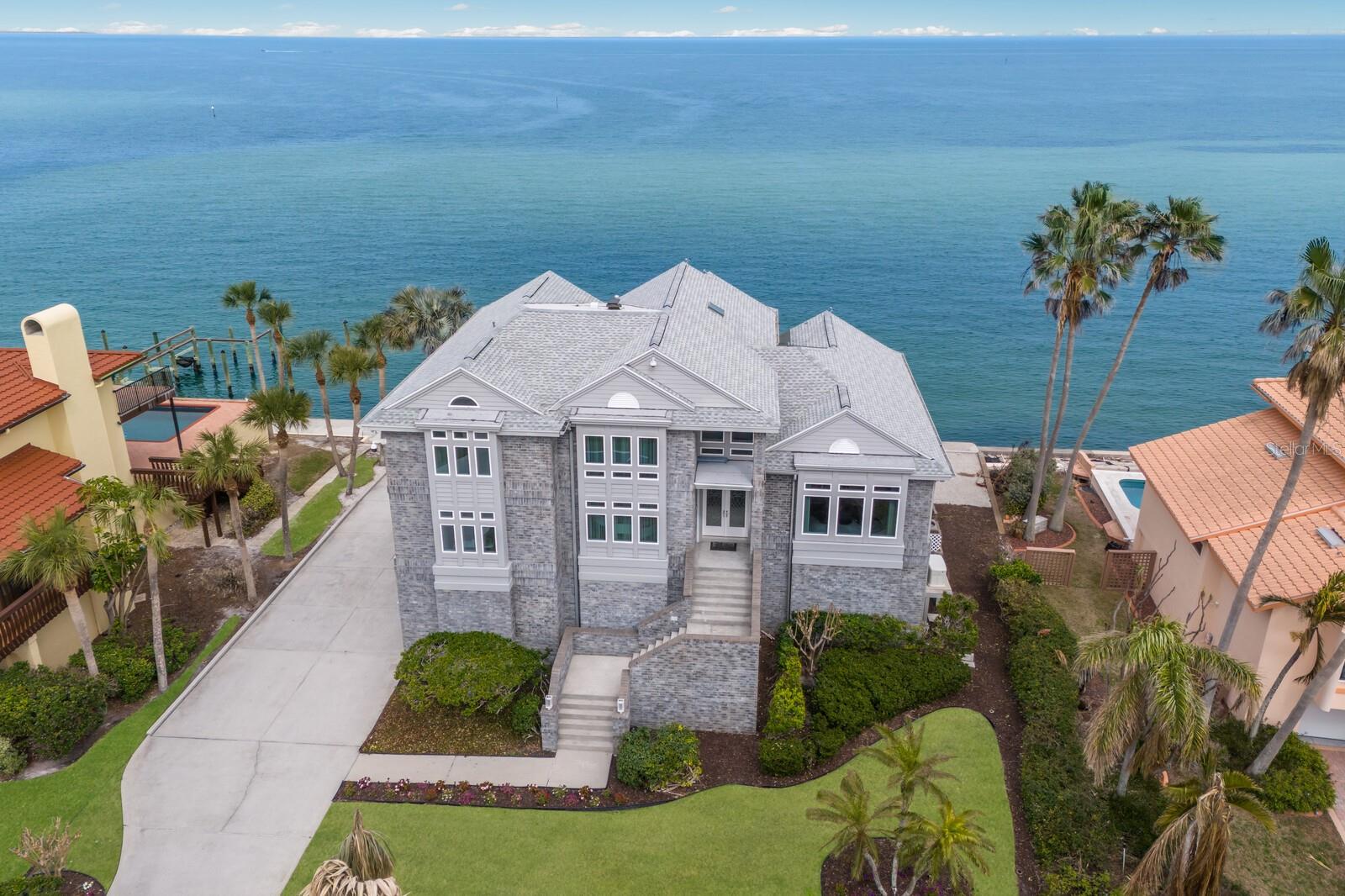 Never flooded—even during major storms—this coastal estate offers rare peace of mind, especially during hurricane season. Experience the epitome of coastal elegance in this stunning 4-bedroom, 3.5-bathroom estate, perfectly positioned along the tranquil waters of Tampa Bay. Located in the prestigious Key Royale community, this home offers unparalleled water views, refined design, and an array of upscale amenities, making it the ultimate island retreat.
Step inside to an expansive open-concept layout, where soaring ceilings, abundant natural light, and panoramic bay views create a seamless blend of luxury and comfort. The living area is framed by oversized impact windows, bringing the beauty of the outdoors inside while ensuring peace of mind. A gourmet kitchen features premium appliances, custom cabinetry, and a spacious island, perfect for entertaining.
The primary suite is a private sanctuary on the top floor, complete with a sitting area, mini kitchen, and private balcony offering breathtaking sunrise views over the water. The spa-like ensuite boasts dual vanities, a soaking tub, and a walk-in shower, providing the ultimate relaxation experience.
Designed for waterfront living, this home features a private dock with direct bay access, ideal for boating and fishing enthusiasts. Unwind by the resort-style pool, soak up the sun on the expansive sundeck, or gather with friends and family in the screened lanai, all while enjoying the sight of dolphins and manatees gliding through the water.
Additional highlights include an 8-car garage with A/C, extensive storage space, and a long driveway for ample parking. Situated just minutes from pristine beaches, a private golf course, and top-tier community amenities, this property offers a lifestyle of luxury and tranquility.