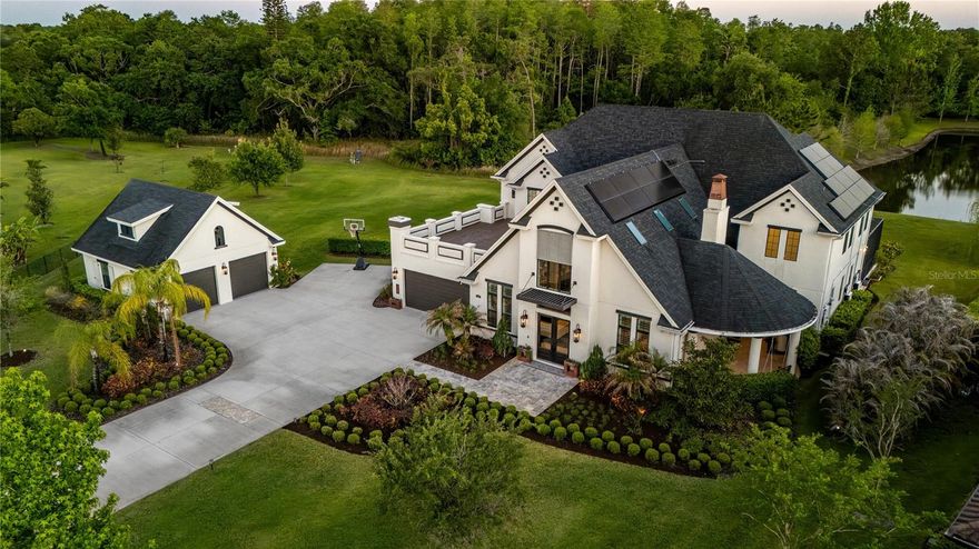 Tucked behind the gates of an intimate enclave of just eleven custom homes, a quiet drive leads you to something truly rare, a residence where scale, design, and setting come together in a way that feels both grand and deeply personal. The long oversized driveway curves toward an exquisite home that dares the imagination of its visitors to wonder what could be inside. As the double doors open, light pours in from above, dancing across the expansive interior and soaring ceilings. Your eyes are ultimately drawn through the home all the way to the rear windows that open to the water and conservation beyond. This is a home that immediately slows you down and invites guests to stay longer. The heart of the home is a stunning chef’s kitchen, anchored by premium Thermador appliances, double pantries, an oversized island, and a built in dining space designed for gathering. It flows effortlessly into the great room, where skylights and custom lighting create a bright yet warm atmosphere, perfect for both quiet mornings and lively evenings. The primary suite is a retreat all its own, privately positioned on the main level with direct access to the pool. The spa inspired bath features separate his and her areas, dual shower heads with a rain feature, and a soaking tub set within the shower, creating a true resort experience. A custom walk in closet is complimented by a dressing niche. Every bedroom offers its own private or direct bath access, giving family and guests a level of comfort and privacy. Upstairs, an entirely separate living experience unfolds with a spacious loft ideal for a media room or game space, along with an oversized outdoor balcony that captures peaceful views of the property. Once outside and the lifestyle continues. The backyard was designed to entertain without compromise. Travertine decking, a custom pool and oversized hot tub, outdoor kitchen, and a statement fireplace all sit beneath an expansive screened enclosure with ambient lighting. Whether hosting a full gathering or enjoying a quiet evening, the setting feels like a private resort. The pie shaped lot opens up to a massive side yard, while the extended driveway and multiple garage spaces, including a separate oversized two car garage, provide flexibility for car enthusiasts, storage, or recreation. This home is as intelligent as it is beautiful, featuring a full Elan smart home system, whole home filtration, reverse osmosis water, hardwired internet throughout, Tesla solar panels with four power walls, and thoughtfully designed upgrades at every turn. From the separate side tea patio to the peaceful water views out back, every detail was curated with intention. This is more than a home it is a place to gather, to recharge, and to live exceptionally.