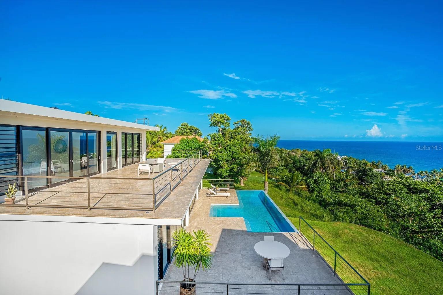 Welcome to Casa Azul—a modern sanctuary of luxury and sophistication in the vibrant town of Rincón, on Puerto Rico’s stunning west coast. Perched atop a secluded hill on an exclusive private street, this tropical paradise is an architectural masterpiece where contemporary design meets effortless functionality.
Designed by renowned architect Sarah Strauss, this breathtaking residence offers 5,000 sq. ft. of gross living area and 3,000 sq. ft. of terraces and pool space, totaling an impressive 8,000 sq. ft. of seamless indoor-outdoor living. Expansive and filled with natural light, the home’s open layout and minimalist aesthetic create an inviting atmosphere designed to enhance its panoramic ocean views. From every angle, you’ll be captivated by the beauty of nature—crashing waves, migrating whales, and unforgettable sunsets.
Step inside, and you'll be greeted by soaring ceilings and a thoughtfully designed footprint that exudes elegance and spaciousness. Floor-to-ceiling glass windows bathe the interiors in natural light while offering uninterrupted vistas of the ocean beyond.
At the heart of this extraordinary home is the expansive pool area, perfect for relaxation and entertaining. Picture yourself basking in the sunshine, feeling the ocean breeze, and listening to the rhythmic waves. The rooftop terrace provides a magical setting for gatherings, leisure, and stargazing.
Each spacious bedroom features its own beautifully designed en-suite bathroom with double sinks and a luxurious soaking tub. For fitness enthusiasts, a state-of-the-art, fully equipped gym allows you to maintain your wellness routine without leaving home.
Every detail of Casa Azul has been meticulously curated for ultimate comfort and style. A top-of-the-line solar energy system and private cistern ensure sustainability and self-sufficiency, providing peace of mind. Fully furnished and move-in ready, this exceptional home invites you to embrace the coastal lifestyle from day one.
Don’t miss the opportunity to own this modern masterpiece in one of Puerto Rico’s most coveted locations.