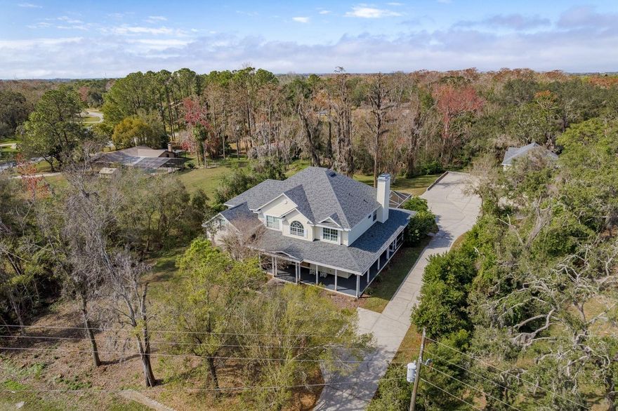 Welcome to Oak Ridge, where this remarkable estate sits on 1.69 acres in the much sought after Trinity area. Offering the perfect blend of peaceful country charm and modern convenience, the property provides room to spread out while still being just minutes from top-rated schools, shopping, dining, golf courses, medical centers, and Gulf beaches. Originally crafted as the private residence of a master builder, the home showcases exceptional quality and attention to detail throughout. With 5 bedrooms, 5 full bathrooms, and 2 half baths, it strikes an ideal balance of elegance and comfort. A long driveway and welcoming wraparound porch create a grand first impression. Just beyond the main residence, a detached 4-car garage includes a spacious studio apartment above, complete with kitchenette and bathroom—perfect for extended family, guests, a private office, game room, or rental opportunity. Inside, freshly stained double entry doors open to a soaring two-story foyer. Hardwood floors carry throughout the main living spaces, where a stone wood-burning fireplace creates a striking centerpiece in the family room. The open-concept layout flows seamlessly into the chef’s kitchen, featuring custom cabinetry with decorative glass accents, a large island, walk-in pantry, and a butler’s pantry that leads to the formal dining room. A casual dining area with French doors offers views of the pool and backyard. The main level also features a luxurious primary suite with French doors opening directly to the pool and hot tub, dual oversized walk-in closets, and a spa-like en-suite bath. An additional bedroom (ideal as an office) and a half bath complete the first floor. Upstairs, another large primary suite includes its own private bath. Two more bedrooms, one with an en-suite, plus a spacious gym (easily converted to another bedroom), private office space, and a loft with laundry chute offer flexibility. A second staircase provides convenient access back to the kitchen. Outdoor living is a highlight, featuring an expansive paver deck, resort-style pool with waterfall, and spa, all surrounded by mature trees and abundant wildlife. A custom-built treehouse, crafted with the same quality as the main home, creates a special retreat for children. At the back of the property, a freshwater creek offers bass fishing and peaceful scenery. With plenty of space for boats, RVs, and recreational toys, this estate combines luxury, leisure, and convenience. Recent improvements ensure peace of mind, including a brand-new roof (2023), newer A/C units (installed within the last three years), a 30kW Generac generator with a 500-gallon underground tank, a water treatment system, plus complete electrical and septic inspections in 2024. Don’t miss the opportunity to experience this extraordinary property—schedule your private showing today!