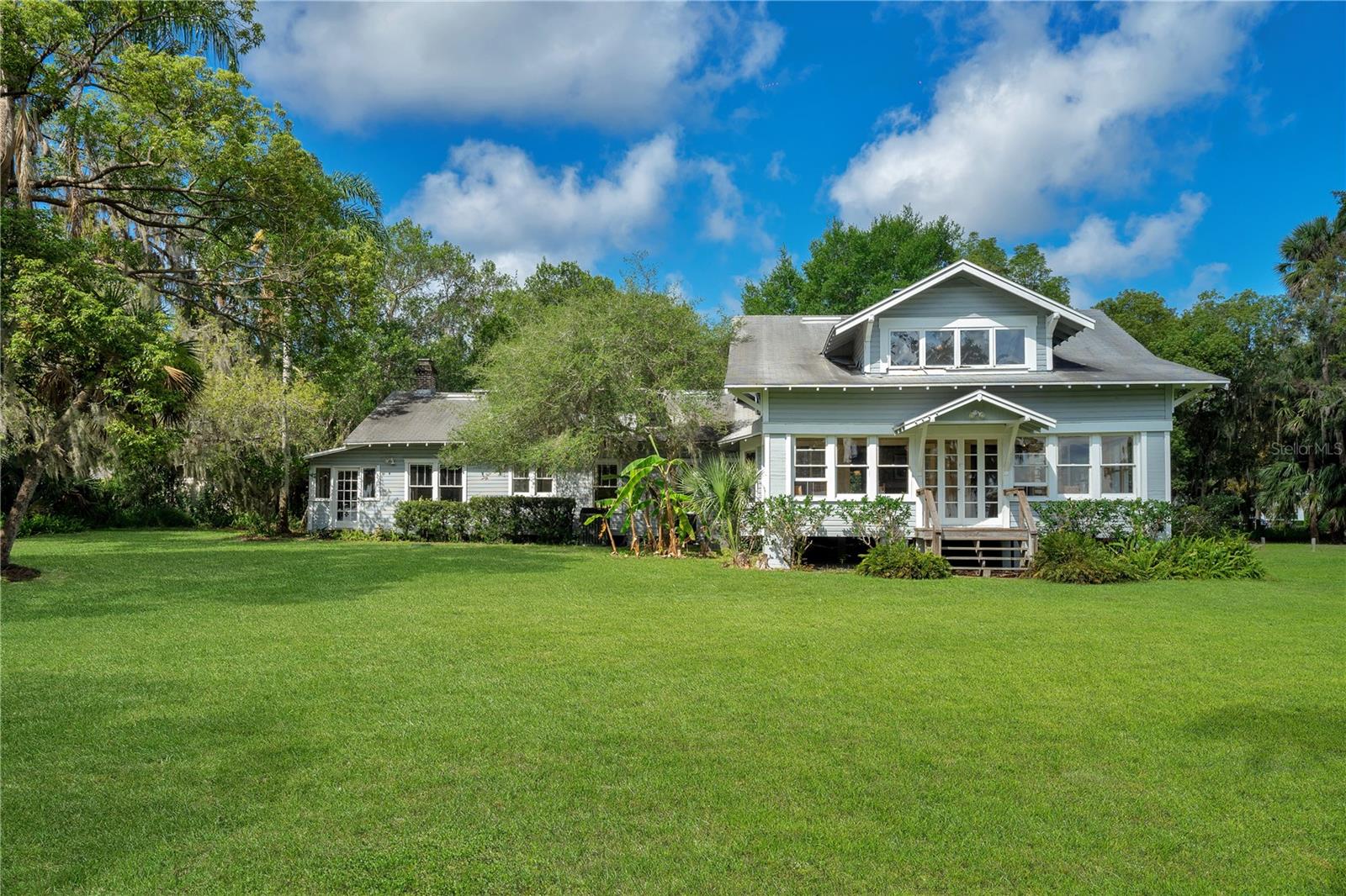 All offers shall be reviewed on Monday, May 1st at 5:00 pm.
Available for the first time in 55 years.
This gracious homestead was built in 1917 and enjoyed by 3 generations of the current owners. It is located off a sand road in Olde Windermere. The large, 1+ acre corner lot gently slopes to Lake Down with 200 ft of sandy shoreline. A canopy of majestic oaks, palms, magnolia and cypress trees frame and shade to welcome all who are lucky enough to visit or dwell here. Chosen in 1999 for filming “Walking Across Egypt”, some of the remnants of the film remain.
Original features include windows, doors and wood flooring. The main home is two story with 4 bedrooms and a walk in attic on the 2nd floor. The square footage does not include additional 500 sf of enclosed porches and detached music studio. The enclosed front porch is lined with windows providing amazing sunrise and water views. A cozy gathering room features beamed ceilings, wood trim, window seating and a brick fireplace. A large formal dining room off the kitchen has a built in corner curio cabinet. Connected by a shared utility room is a 1 bedroom apartment with a full kitchen, living room with fireplace and another enclosed porch. The 20x20 detached garage boasts an additional 15x11 workspace. On the south edge of the property is a separate building currently used as a music room. It is 195 s.f. built for soundproofing and with electric, A/C and Ethernet to apartment. The wall facing the lake was framed for a potential future window making it an ideal home office should one choose. The property has ample parking space for trailers or RV. NO HOA. Keep your boat in the covered boat dock for quick and easy access and enjoyment of all your favorite water sports. The Butler Chain of Lakes is one of Florida’s Outstanding Waterways consisting of 11 interconnecting freshwater lakes. Windermere offers a small town feel just minutes from fine dining, premium shopping, golf and area attractions. From home you can walk to library, parks, restaurant and more. Enjoy weekly Farmer’s Markets and seasonal Town events.
Florida living at its finest!!