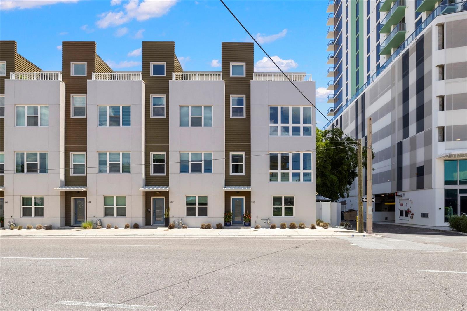 Built in 2018, this Energy Star Certified exclusive end-unit residence in the Skye 333 community blends contemporary design with refined comfort. Featuring 3 bedrooms, 3.5 baths, and 2,150 sq ft of living space, the home is located in a NON-FLOOD, NON-EVACUATION zone and was built by one of St. Pete’s premier boutique builders. Constructed with solid concrete block, hurricane impact-rated windows and doors, and equipped with a tankless gas hot water heater, it offers both peace of mind and timeless quality. Inside, soaring 10-foot ceilings and dramatic walls of glass fill the home with natural light. The gourmet kitchen is the centerpiece of the main living level, designed with a gas range, premium stainless steel appliances, custom wood cabinetry, and an oversized 10-foot island that’s ideal for gathering and entertaining. The primary suite is a serene retreat with two walk-in closets, expansive windows, and a spa-inspired bath with frameless glass shower and dual vanities. Each guest suite includes its own en-suite bath, with a powder bath conveniently located on the main floor.
This is a rare opportunity to own one of only two end-units in Skye 333 that feature both the largest floor plan in the community and a private ground-floor outdoor living area with separate entrance, a distinction that truly sets this home apart. A spacious rooftop terrace offers yet another space to relax or entertain, complete with a covered lounge, wet bar, and sweeping views of downtown St. Petersburg. Additional features include engineered hardwood floors, a full laundry with washer and dryer, smart home technology, and a two-car garage with epoxy flooring and custom storage. Steps from Mirror Lake and the Central Arts District, this residence places you within walking distance of downtown St. Pete’s award-winning restaurants, galleries, and waterfront parks, with easy access to Tampa International Airport and the Gulf beaches. Opportunities like this are exceptionally rare—don’t miss the chance to make this extraordinary home yours.