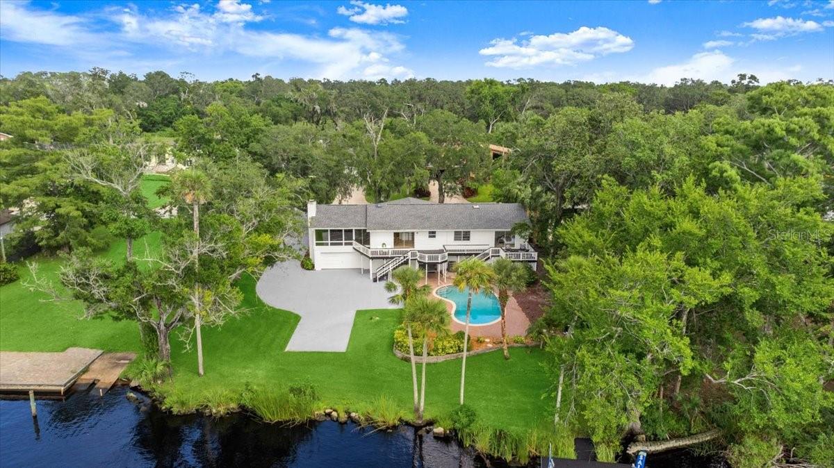 Welcome to 89 N. Saint Andrews Drive, a fully reimagined riverfront estate in Tomoka Oaks Country Club Estates of Ormond Beach. This 4-bedroom, 2.5-bath architectural gem offers 3,849 square feet of elevated living space, masterfully blending mid-century design with luxurious modern comforts, all set along the scenic Tomoka River. Included in the sale is a 37.5 of ownership interest in the adjacent vacant parcel at 87 N. Saint Andrews Drive, an added asset that ensures lasting privacy, enhances your view, and secures shared access to your private boat ramp and fishing dock. With approximately 200 feet of combined river frontage, this property is a true sanctuary for water and nature lovers.
Completely renovated in 2025, the home artfully retains its original charm while embracing contemporary upgrades. Fresh interior and exterior paint, new flooring throughout, energy-efficient dimmable LED lighting, and a Nest thermostat elevate comfort and convenience. A semi-circular drive leads to an under-home garage with ample storage, while mature oaks and lush landscaping soften the home’s bold architectural lines. Functional upgrades, including a new roof, gutters, sump pump, French drains, and expanded garage storage add peace of mind and long-term value.
Step inside the grand double doors into a striking split-level foyer with exposed beams, wood accents, and natural light. The upper-level main living area features a bay window overlooking the front yard and a floating flagstone fireplace set between signature floor-to-ceiling corner windows showcasing sweeping river views. This flexible space easily adapts for entertaining or everyday enjoyment.
The fully remodeled kitchen is both elegant and functional, featuring stainless steel appliances, including a GE Smart refrigerator, built-in oven, and dishwasher, granite countertops, solid wood cabinetry, a central island, and an undermount sink with integrated drying rack. A charming breakfast nook opens onto the rear deck, offering a perfect setting for casual meals or morning coffee. Nearby, a skylit half bath, hidden laundry with new Samsung washer and dryer, and multiple storage closets add to the home’s thoughtful layout.
The serene primary suite offers calming river views, dual built-in closets, and a beautifully updated bath with dual granite vanities, artisan tilework, an oversized rain shower, and a skylight. Sliding doors open to a private deck overlooking the river, your own quiet escape.
Three additional bedrooms each include built-in storage and share a full bath featuring designer finishes and high-end fixtures.
On the lower level, new tile flooring and waterproof PVC baseboards create a versatile space that opens directly to the pool deck—perfect for a game room, creative studio, or additional living area.
Outdoors, a sparkling in-ground pool, expansive deck, and tropical landscaping provide the ultimate backdrop to enjoy Florida’s riverfront lifestyle. Whether lounging poolside, casting a line from the dock, or boating to RiverGrille, the setting is nothing short of idyllic. Just minutes from Tomoka Oaks Golf & Country Club, AdventHealth, The Trails Shopping Center, and the boutiques and cafes of Granada Boulevard, this location balances natural beauty with everyday convenience. With no HOA restrictions, you have the freedom to enjoy this exceptional property on your own terms.