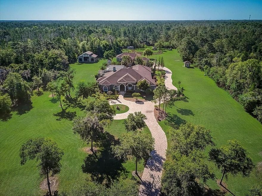 Expansive greenery along a BEAUTIFUL STONE PAVED DRIVE leads the way to this exclusive 9+ acre estate offering 3 bedrooms, 3.5 bathrooms MAIN HOME, a SEPARATE 3 bedrooms 2 bathrooms GUEST HOUSE WITH 2000+SF 10 car garage that is a car enthusiast's dream and a BONUS 2 bedrooms, 2 bathrooms IN-LAW SUITE or POSSIBLE RENTAL SPACE! The elegant and spectacular main house is a socialite’s paradise customized to wow for those elaborate gatherings, yet just cozy enough for a dinner for two. Enter the home for breathtaking views of EXQUISITE WOODWORK, and custom wood hand-carved archways that frame the elite craftsmanship surrounding the large FIREPLACE. This open floor plan with HIGH COFFERED AND TRAY CEILINGS throughout provides an easy sightline from the main family area to an enormous dream kitchen featuring raised cabinets, a stunning massive ISLAND, a butler’s pantry/bar area and breakfast nook overlooking the pool. Take the main living area to the large GAME ROOM WITH A 2ND BAR and walk through custom French doors that suddenly blend indoor and outdoor living seamlessly. The OUTDOOR LIVING SPACE is perfect for entertaining with a massive screened lanai accented with travertine tile, a full OUTDOOR KITCHEN, OUTDOOR FIREPLACE, SALTWATER POOL WITH GROTTO CAVE, JACUZZI, AND FIREPIT. The lanai can also be accessed through the elegant French doors of the spacious master suite featuring a sitting area, his and hers walk-in closets and en-suite master bathroom showcasing split vanities, a fabulous custom stand-alone oval tub, a shower with two huge rain shower heads and handhelds. Other notable features include the whole house water filtration system, irrigation system, new wifi system that allows controlling lighting and temperature for the pool, enormous 2000+SF garage for all of your toys - a car enthusiasts dream!, power hookup for RV, multiple sheds throughout the property, and security system. The beautiful guest house and in-law suite offer the perfect opportunity for multi-generational households or those looking for a turnkey investment option that they can keep a close eye on! This one of a kind estate is truly world class!