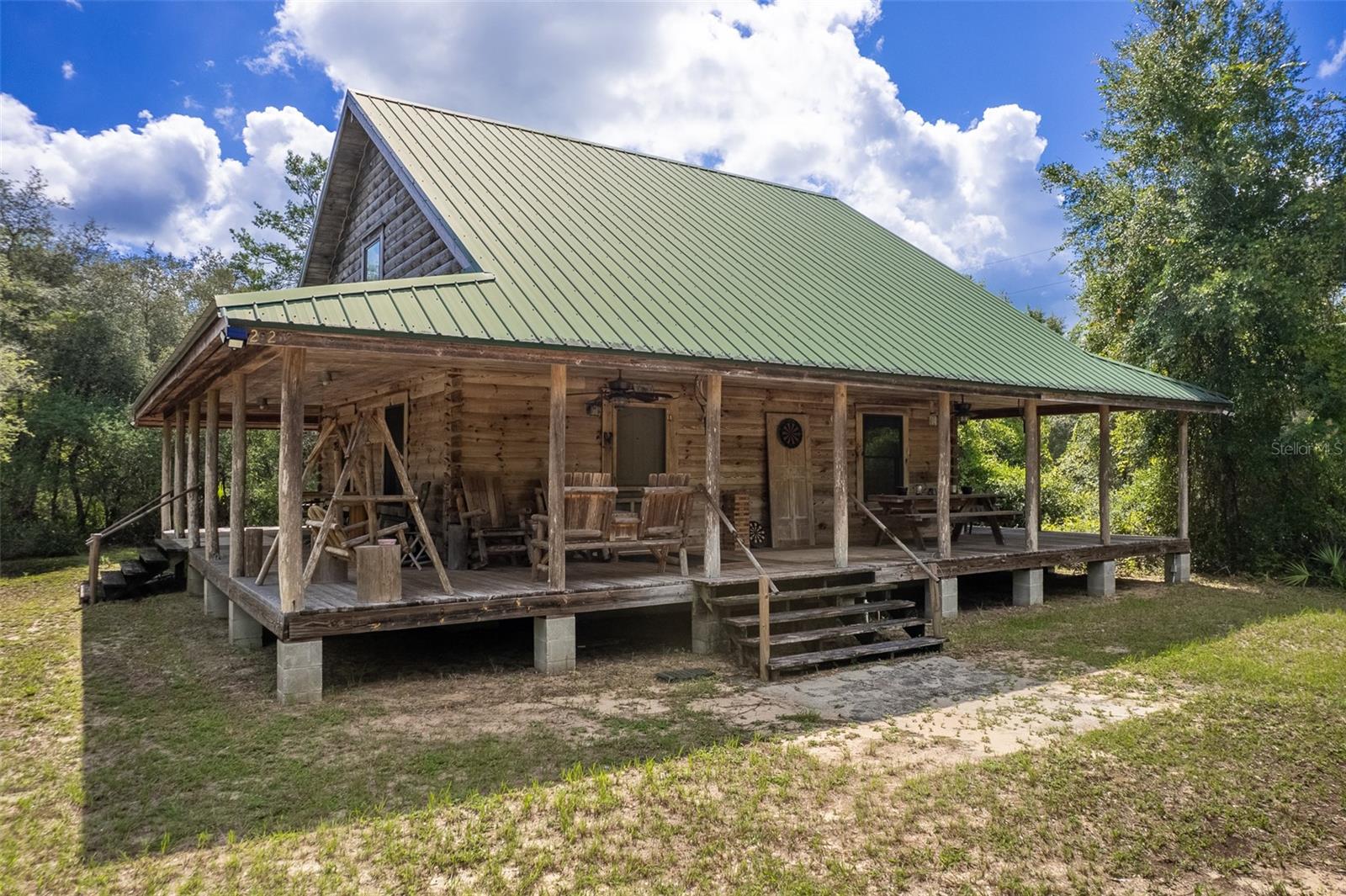 This authentic rustic log cabin retreat is tucked away at the very edge of the Ocala National Forest, offering the rare opportunity to own a property that shares a 340-foot common boundary with the Forest itself. More than just being near the woods, this home places you directly alongside its beauty, giving you immediate access to endless outdoor adventure. The cabin has been carefully designed with the surrounding trees preserved to create privacy and seclusion, giving it the true feel of a hidden retreat. Set on 0.86 acres made up of four lots across two parcels (05269-101-14 and 05269-101-15) , with overall dimensions of 340 feet by 110 feet, the property is large enough to accommodate an accessory building or even another primary structure if desired. According to the construction plans, the first floor offers 720 square feet of living space, with an additional 415 square feet in the loft, for a total interior of 1,135 square feet. The wraparound porch adds 1,304 square feet, bringing the total building floor space to 2,439 square feet.
Inside, all interior walls are tongue-and-groove Southern White Pine, the lower-level floors are Southern White Pine, the bedrooms are finished in warm oak, and the loft is highlighted with rich cherry flooring, creating a timeless blend of natural textures throughout. A log staircase, handcrafted finishes, and abundant woodwork add to the rustic charm you would expect in a true cabin retreat. The home features two bedrooms and a loft bedroom with one and a half baths, plus clever storage options including two attic storage areas and an additional space under the stair landing.
Modern comforts blend seamlessly with the cabin’s character, including a microwave, range, refrigerator, garbage disposal, stackable washer and dryer, ceiling fans throughout, a tankless electric water heater installed in 2021, and an HVAC system replaced in 2010 with ductwork updated just two years ago. Satellite TV service is installed in all rooms as well as the front porch, making it easy to stay connected even while enjoying your retreat. Outside, a wellhouse/storage shed serves as a convenient accessory structure. Surrounding the home is a full wraparound porch, the perfect setting for porch swings, rocking chairs, and evenings spent stargazing under Florida’s clear night skies. The cabin will be sold fully furnished, excluding all taxidermy mountings and a few other personal exceptions, making it easy to move right in and start enjoying. A seven-minute drive takes you to Ferry Boat Landing with its public boat ramp, giving you quick access to Lake Ocklawaha for fishing and boating. Daily conveniences are just a short drive away, with Ocala and Palatka about thirty minutes for larger shopping and dining options. In less than an hour, you can be on the Atlantic Ocean in Daytona Beach or the Gulf of Mexico in Crystal River. Closer to home, you’ll find lakes, rivers, and streams that make this property a true sportsman’s paradise. Whether you envision it as your private getaway, a family retreat, or a profitable Airbnb investment, this one-of-a-kind log cabin blends rustic character, thoughtful design, and unmatched access to Florida’s great outdoors.