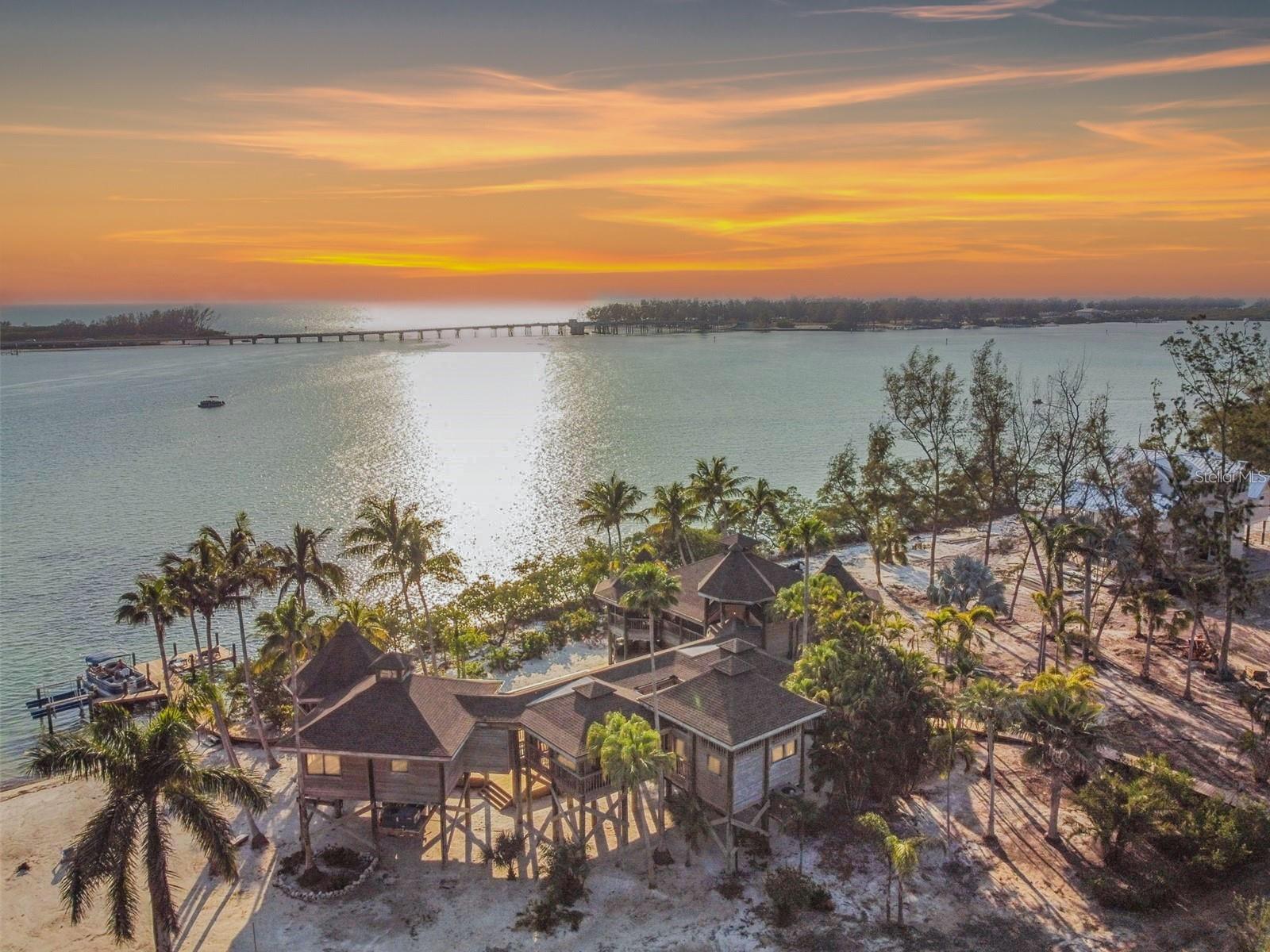 A rare opportunity to own the crown jewel of Florida’s west coast. Tucked away on the private, 38-acre island of Jewfish Key, this extraordinary 1.35-acre estate boasts its own secluded beach and endless views of sparkling aqua waters. Accessible only by boat, this Polynesian-inspired sanctuary offers complete privacy, surrounded by lush tropical vegetation and elevated 18 feet above sea level for peace of mind and panoramic vistas. Designed with a harmonious blend of natural materials and airy, open spaces, the property features raised walkways connecting multiple pavilions. The main residence includes four bedrooms and four-and-a-half baths, while a separate guest suite adds a fifth bedroom and full bath. The newly renovated kitchen is a showcase of modern elegance, with crisp white cabinetry, sleek quartz countertops, and a generous center island—perfect for casual dining and entertaining—flowing seamlessly into the sunlit living area through expansive sliding glass doors. The primary suite is a private haven, complete with a sitting area, bar, wine fridge, and breathtaking views of Sarasota Bay. Its spa-inspired bath offers a soaking tub, walk-in shower, and a serene, light-filled ambiance. Multiple screened porches and wraparound decks invite you to relax in the island breeze. Outdoors, enjoy a brand-new pool and spa with a sun shelf, a spacious sundeck overlooking the iconic Jewfish Key Sandbar, and a private dock with a jet ski lift for effortless access to fishing, kayaking, snorkeling, or simply exploring the surrounding waterways. Longboat Key and Anna Maria Island are just minutes away by boat, offering world-class dining, shopping, and entertainment. Whether as a luxurious personal retreat or an exceptional investment, this one-of-a-kind property delivers the very best of island living—where adventure, seclusion, and natural beauty converge in perfect harmony.