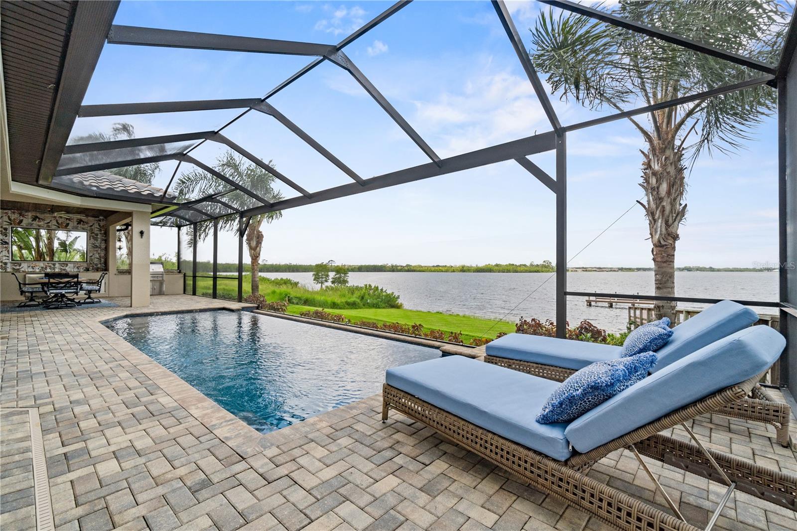 LUXURY LAKEFRONT SHOWPLACE IN THE BEAUTIFUL WATERFRONT COMMUNITY OF WATER RIDGE – WELCOME TO 527 ADAMS VIEW LANE:
Set along the pristine shores of Lake Van in Auburndale FL, this remarkable 4-bedroom, 3-bath lakefront masterpiece is one of the most beautifully designed and meticulously appointed waterfront residences in all of Auburndale. Privately nestled within the prestigious, amenity-rich community of Water Ridge, this 3,800+ sq. ft. home is the perfect fusion of architectural elegance, thoughtful design, and modern luxury—crafted to impress at every turn.
From the moment you arrive, the exterior exudes distinction with its tile roof, custom corbels, manicured landscaping, and striking iron entry gate and doors. Inside, a grand 10’ crystal chandelier sparkles over the custom-tiled foyer, where a wood barrel vault arched ceiling elegantly guides you toward the great room—a stunning architectural detail that elevates the entire entry sequence. Every space has been professionally designed and decorated with exquisite detail—custom millwork, specialty ceilings, hand-selected wallcoverings, fine lighting, and carefully curated hardware create a seamless, polished aesthetic throughout.
The expansive great room is a true showpiece, with soaring ceilings and a wall of glass sliders that frame sweeping lake views and spectacular sunsets. Flowing effortlessly into the formal dining room and gourmet kitchen, this open concept is ideal for both large gatherings and intimate evenings. The chef’s kitchen dazzles with quartz counters, custom cabinetry, silver leaf accent ceiling, stainless steel appliances, gas range, and walk-in pantry.
The first-floor primary suite is a serene retreat overlooking Lake Van, highlighted by a back-lit tray ceiling and elegant chandelier lighting. The spa-inspired bath offers quartz counters, a marble-accented walk-in shower, soaking tub, and hand-painted murals that pay homage to the home’s tranquil lakefront setting. A private guest suite with en-suite bath, a spacious office, and a well-planned laundry/storage area complete the main level. Thoughtful drop stations—one just off the garage entry and another conveniently located off the pool lanai—provide stylish and functional spaces to keep daily essentials neatly organized.
Upstairs, a loft with panoramic water views provides a flexible space for a zen room, game room, or library, accompanied by two additional guest bedrooms and a full bath.
Outdoor living is equally spectacular. A resort-style negative-edge heated pool blends seamlessly with the horizon, while covered lounge and dining areas with a full summer kitchen and granite-topped bar create the ultimate setting for entertaining. A composite walkway leads to the private dock, granting direct access to Lake Van’s clear, sand-bottom waters for boating, fishing, and skiing.
Additional highlights include a 2-car garage with epoxy flooring plus a separate golf-cart/storage garage, Crestron home automation and security system, whole-house Generac generator, tankless water heater and so much more. Residents of Water Ridge enjoy world-class amenities: clubhouse, fitness center, sauna, three pools, tennis and pickleball courts, community boat ramp, and storage facilities. Ideally located less than an hour from Disney and within easy reach of Orlando and Tampa airports, this is a rare opportunity to own a work of art that embodies luxury lakefront living at its finest.
