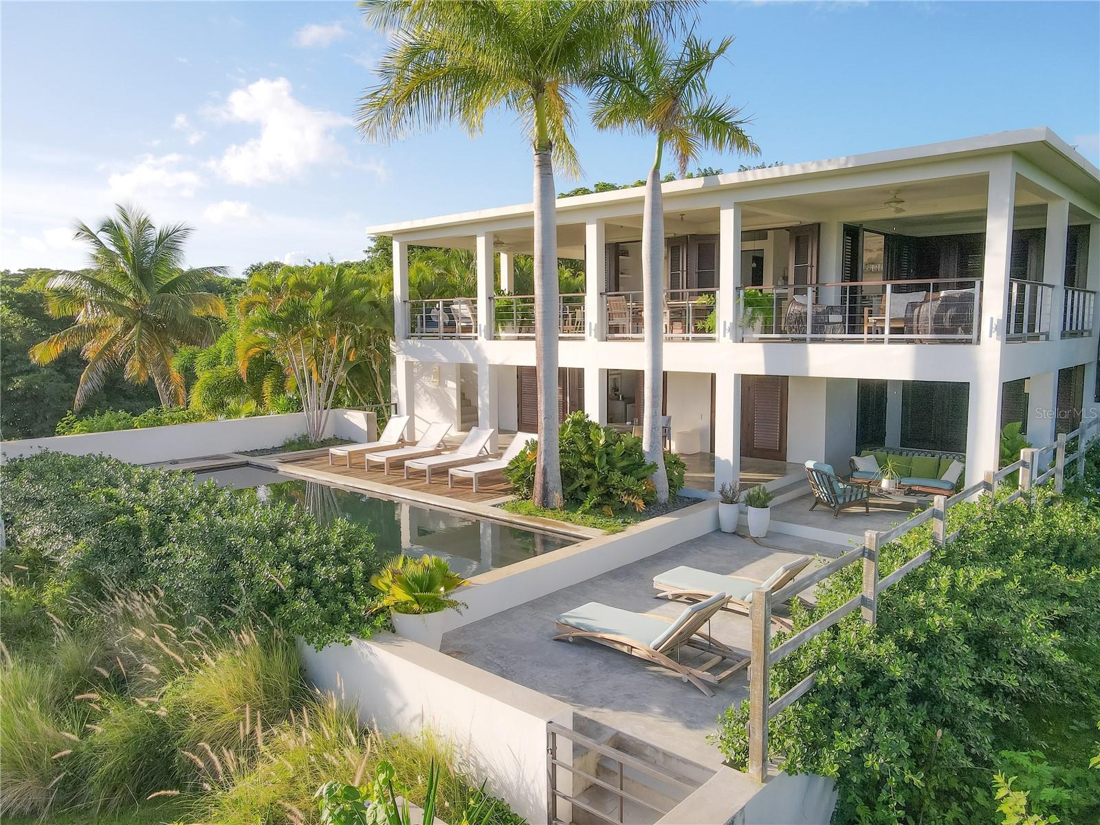 Nestled atop a lush, private hillside in the coveted enclave of El Pilón, Un Poco de Fe is a tropical retreat offering rare seclusion, panoramic Caribbean views, and exceptional income-generating track record . This architectural gem—featured in Coastal Living magazine—is set on nearly three acres of verdant land and is just a short stroll from the acclaimed Finca Victoria Ayurvedic Boutique Hotel & Panchakarma Retreat Center, allowing guests and residents to enjoy wellness and dining amenities in a peaceful, resort-like setting.
Most notably, the villa was recognized by Condé Nast Traveler in 2025 as one of Puerto Rico’s Best, featured among the Best Airbnbs in Puerto Rico – a true testament to its design, setting, and guest experience. The property is being sold fully furnished with curated, imported pieces and a trusted maintenance team in place—ready to continue as a refined private residence, multi-generational retreat, or boutique income property.
A serene tree-lined drive leads to the villa, gracefully positioned at the highest point of the estate. Designed by renowned interior designer Ray Booth, the residence masterfully fuses modern minimalism with Caribbean warmth. Expansive wrap-around terraces, mahogany-framed floor-to-ceiling French doors, and outdoor living spaces blend seamlessly with nature, inviting in ocean breezes, sunlight, and sweeping views of the sea, neighboring islands, and the expansive natural beauty of Vieques.
The upper level of the 4,000 square foot, two-story villa features open-concept living and dining spaces, a bespoke gourmet kitchen with polished cement counters and handcrafted finishes, and a luxurious primary suite with a private sitting room and spa-style bathroom. Every space is thoughtfully oriented to capture the rhythm of the day, from sunrises over the sea to sunsets over the hills.
The lower level includes two additional private bedroom suites, a second full kitchen, an elegant home office, and poolside terraces—ideal for hosting, extended stays, or functioning as a private villa apartment. Each suite offers spa-inspired bathrooms with outdoor showers and direct access to lush tropical gardens and the Diamondbrite gunite pool, reflecting the sky in ever-changing hues.
Surrounded by an established botanical sanctuary of mature palms, flowering bougainvillea, and exotic tropical flora across 3 acres , the grounds exude peace and natural beauty. Top amenities include: a resort-style pool, refined high-design interiors, mesmerizing panoramic views, a serene natural breeze, and expansive green spaces ideal for picnics, entertaining, or simply reconnecting with nature.
The home is fully fenced, partially solar-powered, and equipped with dual entrances, two kitchens, and solar mechanical systems for energy resilience.
Currently operating as a successful luxury vacation rental with a 20-year track record of income, Un Poco de Fe offers a turnkey investment opportunity. With a 4.96 Airbnb rating, it is a consistent guest favorite, celebrated for its thoughtful design, comfort, and serene ambiance. This accommodation is a guest favorite based on ratings, reviews, and its proven reliability. A rare offering combining architecture, nature, wellness, and investment potential— Un Poco de Fe is a Caribbean dream reimagined.
Contact agent to learn more important details. Corcoran PR