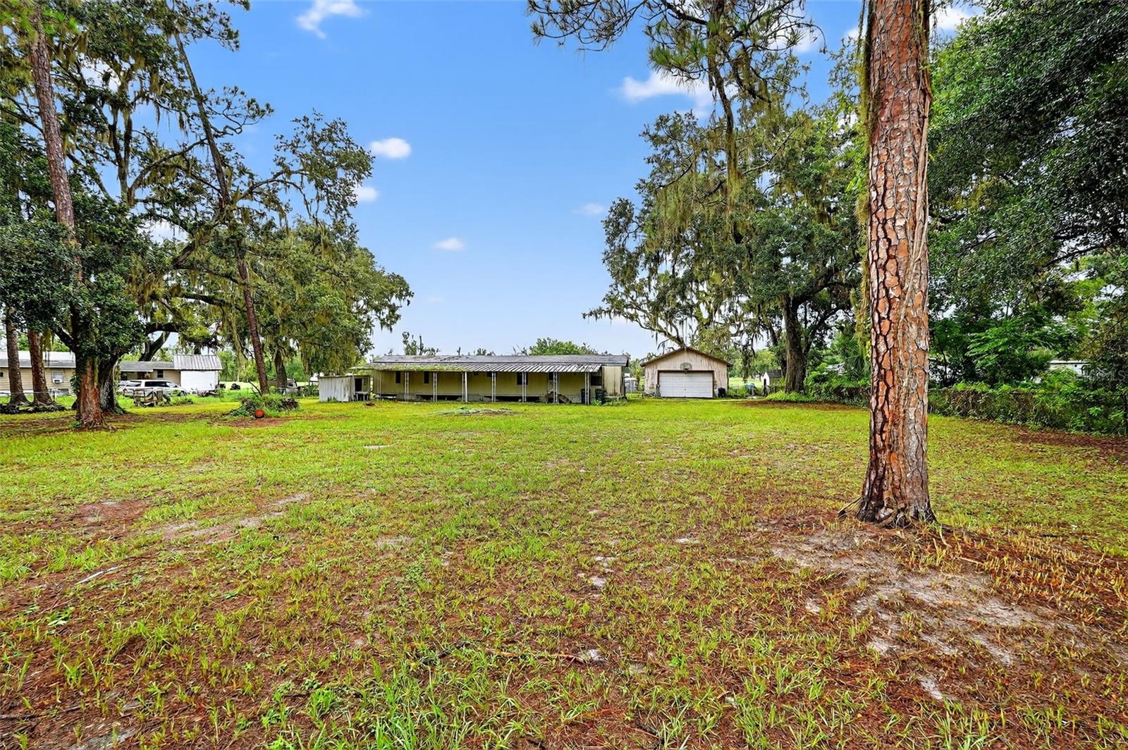 Bring your vision and creativity to this unique opportunity in North Lakeland! Situated on nearly one acre (0.90 acres), this property is fully fenced and shaded by a mix of mature oak and pine trees, creating a peaceful, private setting that feels like country living while still being only minutes from the city. The lot offers 150 feet of frontage and plenty of depth, giving you endless possibilities for designing your next home site, outdoor living areas, gardens, or space for pets, boats, and RVs.
The property currently includes a 576 sq ft block detached 4 car garage, which may be worth repairing or repurposing for a workshop, parking, or storage. The existing single-wide manufactured home conveys in “as is” condition and will require significant work, but that’s where the opportunity lies. Whether you’re looking to replace it with a new manufactured home, build a custom residence, or hold the land as a future investment, this property offers the flexibility that comes with living in unincorporated Polk County with no HOA restrictions.
Location is key, and this property delivers – tucked away on a quiet street but with quick access to I-4, shopping, dining, and schools, making commuting to Tampa, Orlando, or downtown Lakeland simple and convenient. North Lakeland continues to grow, and larger parcels like this are becoming harder to find. This is your chance to secure a property with space, privacy, and incredible potential in one of Central Florida’s fastest-growing regions.