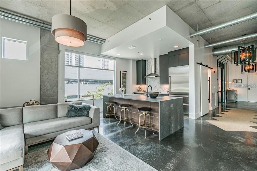 Corner unit in Victory Lofts with that perfect mix of industrial edge and high-end polish. Thoughtfully upgraded throughout, the kitchen is outfitted with a Sub-Zero refrigerator, Wolf gas range, and Asko dishwasher, all complemented by Restoration Hardware lighting, custom quartz concrete countertops (2019), and sleek custom cabinetry (2019).

The space leans into its loft aesthetic with polished concrete floors, soaring 12-foot exposed concrete ceilings, and industrial-style HVAC ductwork, while still feeling elevated and refined. Remote-controlled power shades add a modern touch, and a custom industrial metal and glass wall system (2019) creates both separation and statement.

The bathroom was fully reimagined in 2019 with custom finishes and concrete tile floors, paired with fresh paint and upgraded baseboards throughout the home. 

Victory Lofts offers secured building access and parking, onsite fitness facilities, and a rooftop terrace with a clubroom—ideal for entertaining or unwinding with beautiful sunset views of the city. All of this just moments from Water St, Benchmark Arena Crunch Gym, Publix, Sparkman Wharf, the TECO Streetcar, the Florida Aquarium, and the Tampa cruise port.

Includes one garage space. Available furnished upon request.