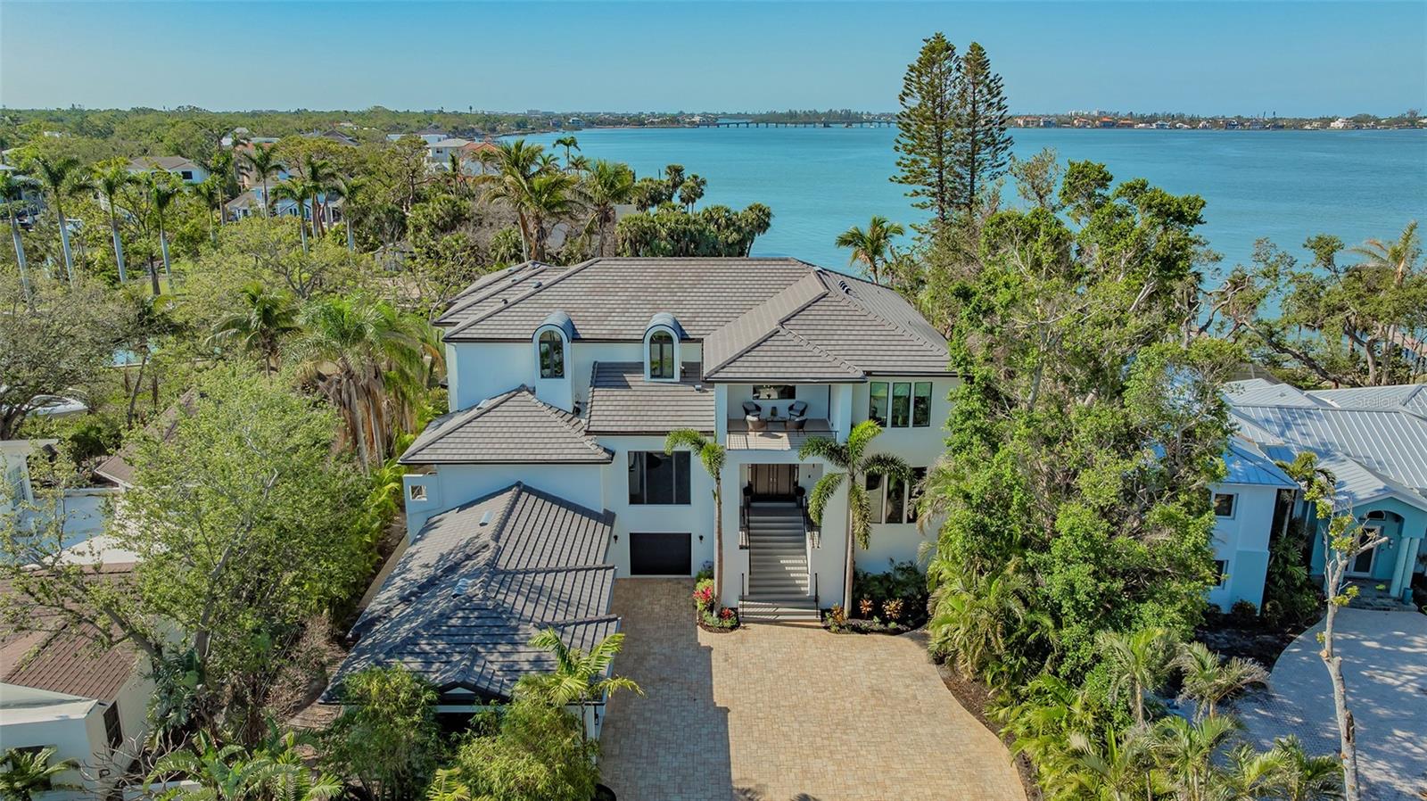Nestled in the prestigious Harbor Acres, this exceptional 4-bedroom waterfront estate embodies the pinnacle of luxury living. Boasting 100 feet of prime bay frontage with a private dock, this masterpiece offers breathtaking, unobstructed views and seamless access to Sarasota Bay. A grand staircase welcomes you into a light-filled, open floor plan designed for both elegance and comfort. Expansive windows frame stunning water vistas, enhancing the bright and airy ambiance. Each generously appointed bedroom features an en-suite bath and walk-in closet, with lavish primary suites on both the main and upper levels for ultimate privacy and flexibility. The gourmet eat-in kitchen is a chef’s dream, complete with top-tier appliances and a striking double-sided gas fireplace shared with the inviting living room—perfect for effortless entertaining. Additional highlights include a sophisticated wine room, an elegant formal dining room, and a stylish family room. An elevator ensures ease of movement between floors, while the private gym, warmed by its own double-sided gas fireplace, offers a serene retreat for wellness and relaxation. Step outside to an exquisite resort-style backyard, where a stunning saltwater pool, multiple terraces, and a spa-like ambiance create the perfect setting for enjoying Sarasota’s idyllic waterfront lifestyle. The outdoor kitchen is ideal for alfresco dining, while the professionally landscaped grounds lead to a seawall and boat dock for direct bay access.
With abundant parking in the spacious four-car garage—complete with an electric charging station—this estate seamlessly blends opulence with modern convenience. Perfectly situated near Sarasota’s renowned beaches, fine dining, vibrant arts scene, and top-tier medical facilities, this residence offers an unparalleled living experience in one of the most coveted waterfront communities