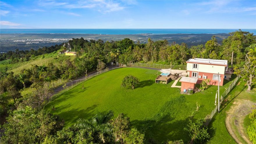 "The Sky House" is situated within a private, gated community, offering over one acre (4,126 square meters) of carefully maintained grounds that ensure privacy and security. The residence, featuring three bedrooms and two-and-a-half bathrooms, is adjacent to El Yunque Rain Forest and provides sweeping, unobstructed views across the Atlantic Ocean, mountains, valleys, and San Juan city. Despite its tranquil and secluded setting, the property is conveniently located only 30 minutes from SJU Airport and San Juan.
A 25-minute walk along a wide jungle path leads to a sizable, discreet swimming hole, fed by a river and bordered by natural boulders. Within five minutes’ drive, residents can access several rivers, hiking trails, waterfalls, and additional swimming sites. The nearby country road connects to renowned oceanfront golf resorts, premium accommodations, dining venues, bars, and beaches along the north shore. This residence presents a distinctive living or investment opportunity. Owner financing available