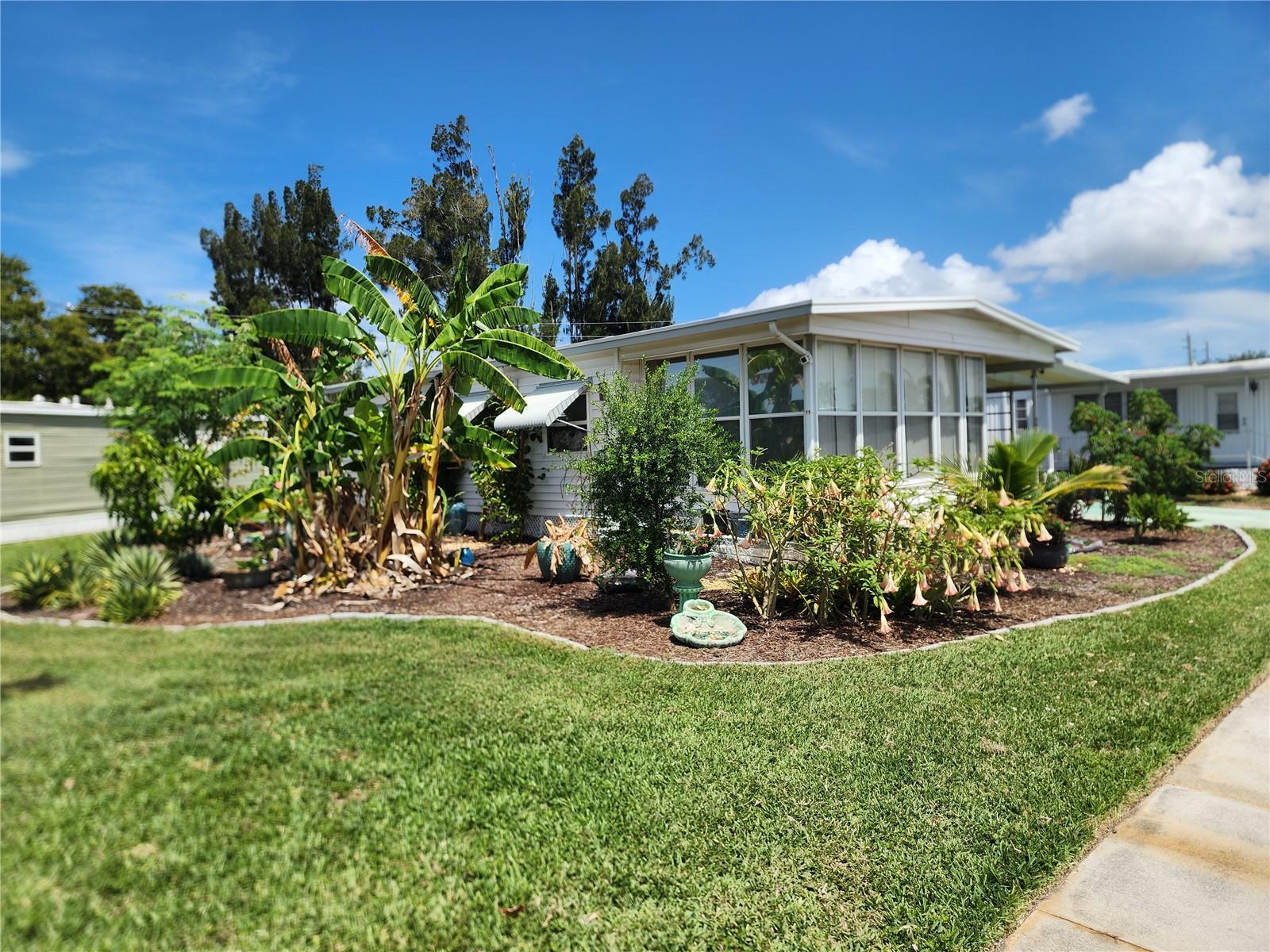 Tucked gracefully on one of the largest corner lots, this property unfolds like a living canvas—its architecture and landscape in constant dialogue with the elements. A mature, self-sustaining garden wraps the home in shades of green and purpose, flowering with pollinator-friendly native flora and fruit trees that tell their own story—banana, soursop, mango, fig, and the tart intrigue of fingerling lime. It is less a yard, more a quietly humming ecosystem.
Step into the kitchen and you enter a space completely reborn. Gutted and reimagined in June 2024, it now stands as a culinary atelier: custom all-wood cabinetry, a gourmet faucet, and a deep sink set with an integrated dish drainer, strainer, and cutting board. A suite of stainless steel appliances—stove, microwave, and dishwasher—gleam under bespoke lighting. Below, plumbing is brand new, invisible but essential.
The bathroom echoes the same philosophy of craftsmanship and ritual. Taken down to its barest bones and reassembled with intention: a separate tiled shower and a Japanese soaking tub nest beside custom lighting and a backsplash that blurs the line between utility and art. Beneath your feet, ceramic tiles over cement board hold warmth from the EcoSmart tankless water heater that whispers efficiency.
The house breathes through its updated lungs—windows replaced in thoughtful succession (kitchen 2018, south side 2022, small bedroom 2025), each a frame to shifting light. Electricity has been completely modernized: a new breaker box in early 2024, intelligent switch upgrades in the kitchen and bath, outlets refreshed for today’s needs. The AC, a brand-new installation from June 2025, promises comfort through the heat.
A 5/8" plywood subfloor anchors it all, hidden beneath layers of luxury vinyl. The structure above is protected by a metal roof, its fastenings freshly sealed. New ceiling fans in every room sway gently beneath clean lines.
Weather has left its fingerprints: Hurricane Milton in late 2024 took a swipe at the lanai roof and siding, and Hurricane Debby sent water through a plugged downspout. But the response was swift and thoughtful—floors bleached and sealed, drywall replaced, integrity restored.
Out back, the Bee & Butterfly Garden unfurls like poetry, planted in 2023 and still growing. It's more than beautiful—it’s medicinal, edible, and alive with motion. A living tribute to resilience, regeneration, and the quiet art of intentional living.