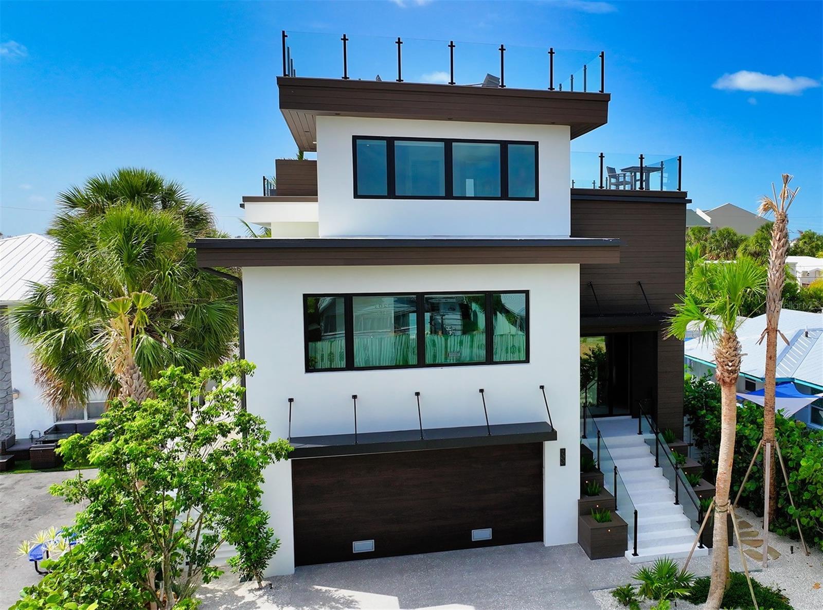 An entertainment mecca on Lido Key, this extraordinary modern retreat embodies the essence of luxurious island living. Built with exceptional craftsmanship, this home stood strong and untouched through recent storms, with no structural or water damage—a true testament to its resilience and quality. Fully furnished with meticulously selected designer furniture, this home boasts luxurious features, state-of-the-art amenities, and an unbeatable location. This is the perfect sanctuary to create lasting memories with your loved ones, generate incredible rental income, or both! Upon arrival, you'll be greeted by tropical landscaping and a meticulously designed exterior. The ground floor features a spacious 2-car garage and a captivating pool area, perfect for relaxation and entertainment. The home is equipped with a commercial-grade elevator, ensuring convenience and easy access to all levels including the rooftop deck. The main living level offers a bright and airy atmosphere, adorned with an abundance of natural light that filters through the open layout. The living room exudes modern elegance, and it is perfect for entertaining or cozy movie nights. The kitchen is a culinary enthusiast's dream, equipped with custom cabinets, Dacor and Bosch appliances, and stunning quartz counters with an expansive waterfall kitchen island with dual dishwashers. The bedrooms epitomize comfort and tranquility, offering a serene retreat after a day of island exploration. Each bedroom features its own en-suite bathroom, ensuring privacy and convenience. The owners suite sits secluded on its own level with a bathroom that makes you feel as if you are in a spa-inspired haven, featuring a large vanity, dual sinks, and a glass-enclosed walk-in shower. The other 5 bedrooms are thoughtfully spread across the additional levels and include a built-in bunk room. The double rooftop on the top deck offers a spectacular setting for entertaining guests while reveling in panoramic views of all aspects of the island including the Gulf of Mexico. Numerous seating areas provide ample space to admire mesmerizing sunsets, while an additional rooftop area offers a serene lounging space. After a day at the beach, cool off and bask in the Florida sunshine by taking a refreshing dip in the resort-style heated pool complete with a water slide. The fenced-in yard, adorned with lush palm trees, ensures privacy and tranquility. You will delight in an unforgettable island experience, with a plethora of exciting activities for everyone to enjoy. Conveniently situated just a short 2-minute stroll from Lido Beach and a mere 5-minute walk to the renowned St. Armands Circle, this home offers unparalleled access to the best of the island lifestyle. Currently enrolled in a luxury vacation rental program, this property can be enjoyed privately or the new owner can continue to take advantage of tremendous rental income when not in personal use.