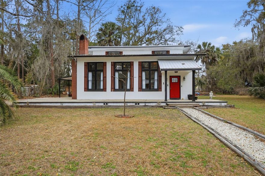 One-of-a-kind and full of character, this Mid-Century Modern-inspired home immediately commands your attention. Thoughtfully updated in 2023, with a metal roof installed in 2018 and a full re-plumb completed in 2025, this home offers the perfect blend of architectural charm and meaningful system upgrades. Drenched in natural light from oversized black-framed windows of every shape and size, the interior celebrates volume, texture, and design. The dramatic main living area features soaring 20-foot ceilings, a stunning balcony overlook, and a massive wood-burning brick fireplace--complete with a built-in wood box--creating the ultimate gathering and entertaining space, with a conveniently located half bath nearby.The primary suite is privately tucked beneath the balcony just off the main living area and features a modest yet stylish en-suite with a walk-in shower and double-sink vanity. Just down the hall, a dedicated office provides the perfect work-from-home retreat. The modern kitchen with gas range flows into a spacious dining room highlighted by a contemporary accent wall, while the walk-through laundry/mudroom adds everyday convenience. Upstairs, two large bedrooms are connected by a Jack-and-Jill bath, offering flexibility for family or guests. Outside, a wraparound concrete patio helps keep maintenance simple while extending your living and entertaining space outdoors. The covered rear patio is ideal for summer barbecues, and the spacious corner lot provides room for boats, trailers, and all your recreational toys. With well and septic service and no HOA, you'll enjoy both independence and functionality--all quietly located in the heart of Palatka just minutes from downtown, the riverfront, and Ravine Gardens State Park.
