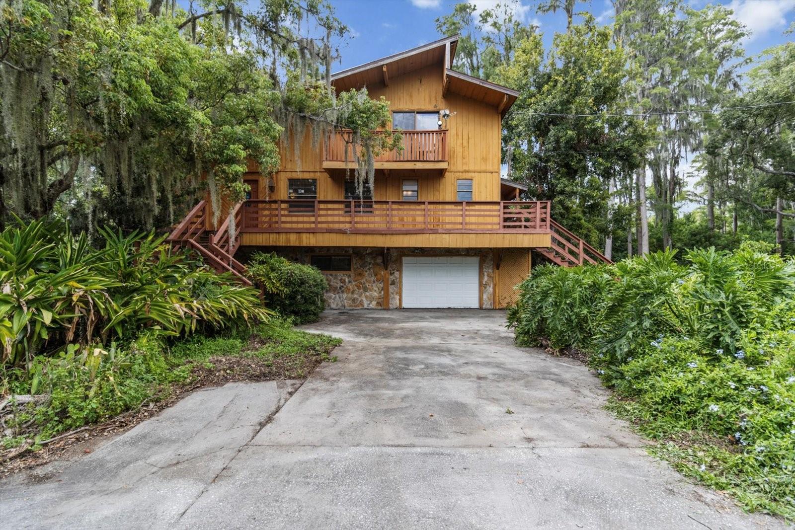 Exceptional Lakefront Estate on Nearly 4 Acres with 350 Ft of Freshwater Shoreline. This rare retreat spans 2 adjoining parcels and offers a unique blend of natural beauty, spacious living, and versatile functionality. Horses allowed. No HOA. No flood insurance required. The primary residence is a striking 3-story contemporary home (built in 1981), designed to capture panoramic views of the lake from every level. Inside the main home, you'll find 3,463 sq ft of living space and a total of 5,472.70 sq ft under roof. The attached 2-car garage features a rare drive-through design, allowing easy access straight through to the backyard and into Little Lake Hobbs, which connects to the 61-acre deep-water Lake Hobbs. The 2nd parcel, located at 417 Trout Lake Ct, includes a 1,280 sq ft concrete block garage with two 8-ft doors, 10-ft ceilings, 4-post car lift, a half bath, extra footings, and wooden trusses—constructed with potential for upward expansion. Whether you're seeking a full-time residence, a multi-generational compound, or a unique investment opportunity, this lakeside estate is truly rare and remarkable. The 2nd floor is the heart of the home, featuring a great room with vaulted ceilings and Canadian cedar beams, a floor-to-ceiling stone fireplace with gas logs, an eat-in kitchen, a dry bar with cedar shelving, a dining area, and an atrium breakfast nook. Additional features include a walk-in closet at the entry, a rec room, a half bath, and a laundry room with a built-in ironing board. The ground-level in-law suite has its own entrance, full kitchen, laundry room, walk-in closet, bathroom with walk-in shower, and a living area with sliding doors that open to a covered patio, koi pond, and lake views. Upstairs, the 3rd floor hosts the primary suite and 2 guest bedrooms. The primary suite includes a large walk-in closet with a window and exhaust fan, a jetted tub encased in glass, a walk-in shower, bidet, high-rise commode, and vanity. The guest bathroom features a steam bath with a Jacuzzi tub. Outdoor living shines with a screened patio and 6-person Jacuzzi, and a 2nd-level balcony with elevated lake views connected to the 3rd-level deck via a circular staircase. A metal-roofed pole barn and multiple parking pads accommodate boats, RVs, or equipment. A Ford tractor with bush hog is included (needs repair). The estate is fenced with electric front fencing and features a pecan grove, Bahia pasture, avocado, cherry, papaya, and mulberry trees, as well as grapevines. A cement bench offers shaded lake views. Additional Features: Outdoor lighting, Well-fed irrigation, 300-ft deep well with 3HP submersible pump, 100-ft backup well, Propane instant water heater and attic fan on the third level for energy efficiency. Water enthusiasts will love the covered boat dock with sundeck, boat lift, launch, outdoor lighting/electric outlet, and stairway access from the home just a few feet away. Conveniently located just 20 minutes from downtown Tampa, with easy access to the Suncoast Pkwy, Van Dyke Rd, and Dale Mabry Hwy. Commute times: 21 mins to Tampa VA Hospital, 22 mins to Tampa Airport, 36 mins to MacDill AFB, 20 mins to USF, and under 1.5 hrs to Orlando Airport.