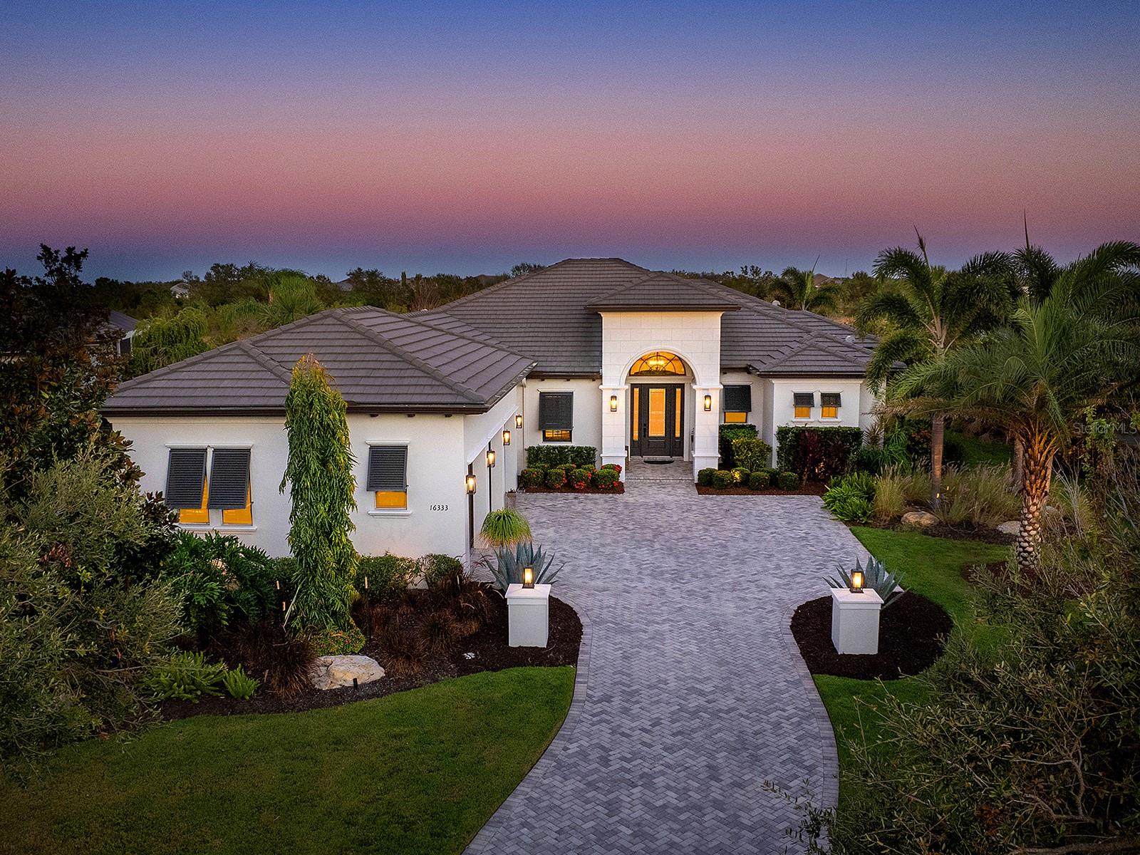 Warm, inviting, private – the words that best describe this stunning John Cannon home in The Lake Club of Lakewood Ranch. The house is set back from the road on .42 acres, bordering a lush Florida preserve. This 2019 Talia floor plan has had every detail carefully chosen using natural materials- brick feature walls, exposed wood beams and wood-look porcelain plank tile flooring. Meticulous landscaping and specimen trees line the curved paver driveway. The covered front landing, with an impact glass door, opens into the spacious, high ceiling foyer. The entertaining areas are positioned to highlight the endless conservation views. This protected preserve is home to deer, heron and sandhill cranes. The central Great Room is designed for comfortable gathering and features a custom tray ceiling, entertainment and display niches, brick feature walls and sliding glass doors to the lanai. The Dining Room, with its exposed wood beams and disappearing corner sliders, has an open flow into both the indoor and outdoor kitchens and is functional and beautiful for both casual and formal dinners. The paved lanai is a peaceful place to enjoy the view. It is furnished with designer lighting fixtures, a well outfitted outdoor kitchen and a heated, Gunnite/Pebble tec saltwater pool and spa. The lanai is secured by a colonnaded screen enclosure. Behind the lanai is a beautifully landscaped backyard space. The same natural finishes, brick walls and wood beams extend into the chef’s kitchen. The kitchen features a wall of windows that let in natural light throughout the day. The large central island has a beautiful, Cambria quartz countertop. The kitchen is built for entertaining, with Chef quality stainless steel appliances including a Bluestar professional-grade 6 burner range, 48” Sub Zero refrigerator, double Bosch ovens, two Bosch dishwashers, ample storage in sleek modern cabinetry that extends to the ceiling and a spacious walk-in pantry with custom shelving, hidden behind cabinet doors. Enjoy the view of the pool, lanai and preserve from the relaxing primary suite with designer feature wall, plush carpeting and dual walk-in closets with custom shelving and ample hanging space. The same attention to detail is evident in the spa-like bathroom with designer wallpaper, long vanity, large walk-in shower, modern cabinetry and fixtures. Guests will enjoy the two en-suite guest bedrooms with walk-in showers and designer lighting. This open floor plan includes a large bonus “club” room with sliding glass lanai doors, powder room, huge storage closet with custom shelving, office space with built-in desk and laundry room with extra cabinetry. The custom, 3-car side-loading garage is an enthusiast’s dream. 3 8000-lb capacity Atlas vehicle stackers expand the space to accommodate up to 6 vehicles. Vehicles up to an 80” SUV can easily fit under a stacker. A 2022 mini-split AC unit and Icynene spray foam insulation maintain a constant temperature. The vehicle stackers can also be used as extra space for temperature-controlled storage. In addition to John Cannon’s quality construction, this home has impact doors and windows though out, landscape lighting, 2020 Kohler whole-house generator, 2022 Culligan whole-house reverse osmosis water filtration, Clare Home automation with cameras, Sonos surround sound, surge protector and other security features. The Lake Club is a premier, gated community with a Grande Clubhouse, restaurant, pool, tennis, pickleball and more.