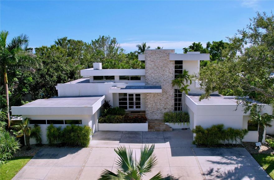 Exceptional Harbor Acres modern residence offering 5 bedrooms, including a sunroom converted by the owners into a true 5th bedroom (closet and A/C). Warm contemporary design with seamless indoor-outdoor living.
Located in Harbor Acres, one of Sarasota’s most coveted neighborhoods, this exceptional modern residence delivers a rare blend of warm contemporary design, luxury finishes, and seamless indoor-outdoor living. Perfectly scaled for the neighborhood, the open floor plan is flooded with natural light and effortlessly blurs the line between inside and out. The great room features 8-ft pocketing sliders opening to the covered lanai, anchored by a gas fireplace with illuminated floating shelves. The chef’s kitchen is a showpiece with top-of-the-line Miele appliances, solid wood cabinetry, an expansive quartz island, LED lighting, and a butler’s pantry for effortless entertaining. A separate dining room with picturesque windows offers an inviting setting for intimate gatherings, while the adjoining family room provides a relaxed space to unwind.

The first-floor primary suite is a serene retreat with walls of windows overlooking lush tropical foliage and a spa-inspired bath featuring a soaking tub and glass shower. A dedicated office/flex room is conveniently located on the main level. Owners thoughtfully converted the sunroom into a 5th bedroom, offering added flexibility for guests or multigenerational living. Sleek open-riser stairs lead upstairs to two en-suite bedrooms providing privacy and comfort.