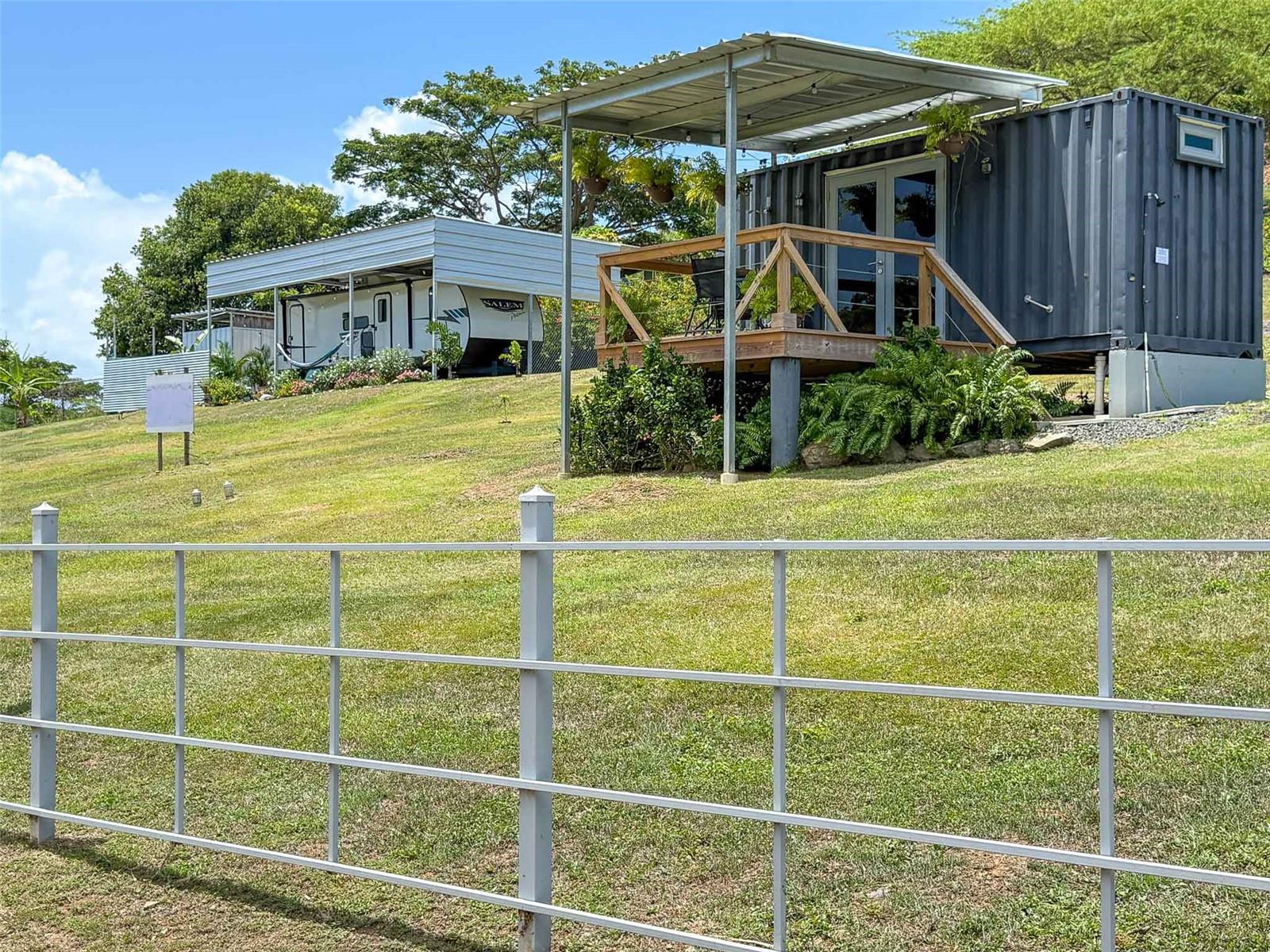 Tres Corazones is a unique, turnkey property located in Villa Borinquen on the island of Vieques, Puerto Rico. This thoughtfully designed compound includes two stylish sleeping structures, an additional full bath/laundry outbuilding, two outdoor soaking tubs, and on-grid utilities, offering flexibility for personal use, vacation rental income, or both.
The primary structure is a Forest River Salem Platinum RV (26DBUD floorplan) permanently installed on a concrete pad and protected by a custom-built metal roof. Inside, the RV features a queen-size primary bedroom with built-in closets, a cozy lounge area with decorative fireplace and TV, a full kitchen, dining space, bunk beds, and a full bathroom. Large windows throughout bring in natural light and frame the surrounding tropical landscape. The RV is fully air-conditioned and comfortably sleeps up to six.
Just a few steps away is the second structure—a professionally converted shipping container home with queen bed, full kitchen, full bathroom, and covered wooden deck. This unit also features an outdoor shower and satellite TV, making it ideal for guests or renters seeking privacy and comfort.
The third structure on the property contains a second full bathroom and a laundry area with washer and dryer. A deep metal soaking tub adds charm to the space, while a second outdoor bathtub is tucked into a private corner of the property for evening stargazing or post-beach relaxation.
The lot includes public water, electric service, and septic system. The landscaping offers a mix of shade and open sky, perfect for outdoor living and dining. The structures are well-maintained, and the layout is optimized for privacy, functionality, and island living.
Tres Corazones has also proven itself as a strong income-generating short-term rental. It ranks in the Top 5% of most-loved homes on Airbnb in Vieques and has earned consistent Superhost recognition. It is being sold fully furnished and ready to operate as a turnkey investment.
Located just a short drive from the ferry terminal, beaches, shops, and restaurants, this property puts you close to everything yet offers a sense of retreat. Enjoy easy access to Playa Caracas, Playa Negra, and the world-famous Bioluminescent Bay, as well as popular dining spots in Isabel Segunda and Monte Santo.
If you're looking for a creative, flexible, income-ready property in Puerto Rico, Tres Corazones offers an ideal blend of style, functionality, and Caribbean charm.