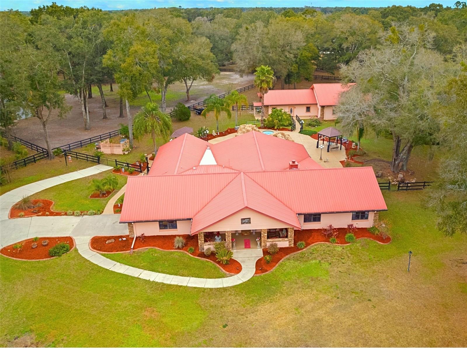 One or more photo(s) has been virtually staged. *PRICED BELOW APPRAISED VALUE + HOME WARRANTY INCLUDED!* This is a private, GATED community on 3.18 fully fenced acres with AG zoning, minutes from the World-FAMOUS Equestrian Center! With 6 total BEDROOMS and 3.5 baths, the main house features vaulted ceilings, wood beams, dual HVAC, split floor plan, and multiple walk-in closets. The CUSTOM SPORTS BAR overlooks 2,000+ SF of breezy porch space, seamlessly blending into a RESORT-STYLE POOL with a HEATED SPA, creek, waterfall, and natural rock ledge. The scenic walkway leads to a 2,600 SF detached garage with 3 OVERSIZED BAYS, its own HVAC, septic, attic, one of three 200-amp electrical panels and a GUEST house with full bath, kitchenette, and 1,000 SF of additional covered CARPORT parking! Every bell, every whistle—THIS ESTATE HAS IT ALL!!