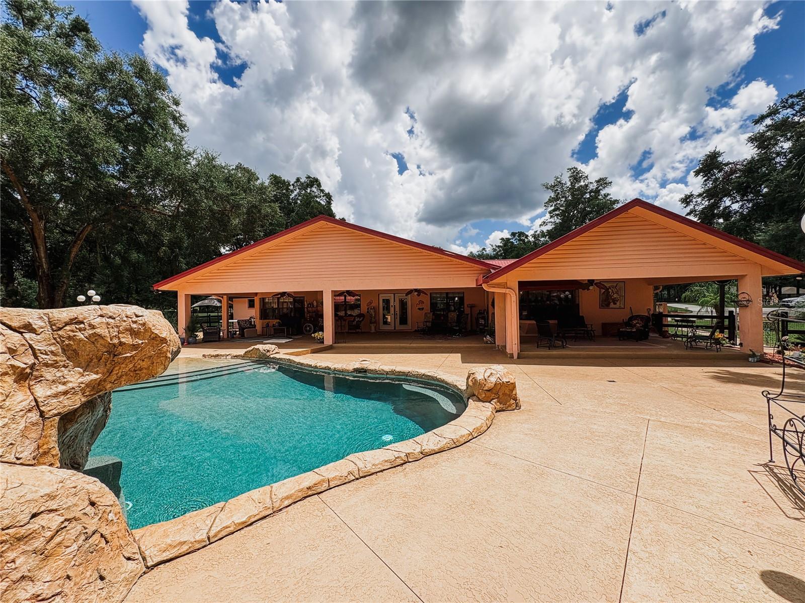 One or more photo(s) has been virtually staged. *PRICED BELOW APPRAISED VALUE + HOME WARRANTY INCLUDED!* This is a private, GATED community on 3.18 fully fenced acres with AG zoning, minutes from the World-FAMOUS Equestrian Center! With 6 total BEDROOMS and 3.5 baths, the main house features vaulted ceilings, wood beams, dual HVAC, split floor plan, and multiple walk-in closets. The CUSTOM SPORTS BAR overlooks 2,000+ SF of breezy porch space, seamlessly blending into a RESORT-STYLE POOL with a HEATED SPA, creek, waterfall, and natural rock ledge. The scenic walkway leads to a 2,600 SF detached garage with 3 OVERSIZED BAYS, its own HVAC, septic, attic, one of three 200-amp electrical panels and a GUEST house with full bath, kitchenette, and 1,000 SF of additional covered CARPORT parking! Every bell, every whistle—THIS ESTATE HAS IT ALL!!