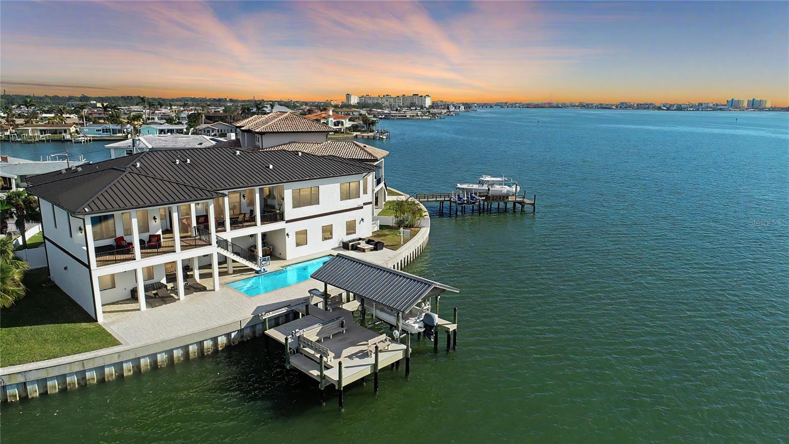 Discover unparalleled privacy and waterfront living in this exceptional custom-built Spanish/Mediterranean masterpiece, located in the prestigious Oakhurst Shores neighborhood of Seminole, FL. Built hurricane-proof with hurricane windows, breakaway walls, and a whole-house generator, this 2017-built estate stands as a testament to both beauty and resilience. Set on 167 feet of deep water frontage along the intracoastal Boca Ciega Bay, with quick access to the Gulf of Mexico, this estate offers breathtaking views, flawless craftsmanship, and ideal location - just 3 miles from the beach, perfect for coastal living without beach traffic or bridges.
Upon entry through the foyer from one of two garage accesses, you’re greeted with an air-conditioned storage room & the option to take either the private elevator or a stairway to the main living level. The home features an open design with 13-foot high ceilings, four spacious bedrooms (one convertible to an office), a large game room with a custom wet bar, & ample space for relaxation & productivity. Custom wood blinds throughout & remote-controlled shades on back-facing windows provide comfort & style.
The chef-inspired kitchen boasts an expansive island breakfast bar, stainless steel Thermador appliances, double convection ovens, a 6-burner gas cooktop with a griddle, a pot filler, a wine cooler, and a warmer drawer. Additional features include custom cabinets with soft-close drawers, a large pantry, and extensive storage. The primary suite is a private retreat, complete with an enormous walk-in closet with built-in features, an island with additional storage, and a luxurious bathroom featuring a walk-in shower with dual programmable controls for multiple shower heads, his-and-her sinks, and a separate toilet room.
The seamless flow of indoor and outdoor living is enhanced by a massive, covered patio equipped with a custom-built outdoor grill and counter. The backyard oasis includes a saltwater pool that can be heated or cooled & features jets, waterfalls, and multi-colored lights—all operable via phone. The custom removable fence and gates surrounding the pool and seawall provide safety for children and pets. The expansive space also features a fire pit area, wrap-around benches on the dock for enjoying the water views or fishing, and a fenced yard with entry gates on each side.
Boating enthusiasts will appreciate the private dock, equipped with full water and electric service, a fish cleaning station with running water and electric, two boat lifts (currently one for a boat and one as a platform for kayaks/jet skis, convertible to another lift), and built-in seating perfect for relaxing or entertaining.
Luxury and convenience abound throughout the home, which features a 50-year metal roof, an oversized 8-car garage with high, smart-enabled doors accommodating boat storage, a whole-house water softener, a high-pressure water system with salt-free filtration, and an upgraded full manifold for individual shut-offs. Additional highlights include a built-in pest control system, a tankless gas water heater, sound insulation in the family room, kitchen, and laundry, WiFi extenders installed throughout, and a 7-camera security system with an electronics equipment closet.
This home represents an extraordinary Florida lifestyle where every detail has been meticulously crafted to provide luxury, comfort, & ease. Don’t miss this rare opportunity to own a piece of paradise in Oakhurst Shores.