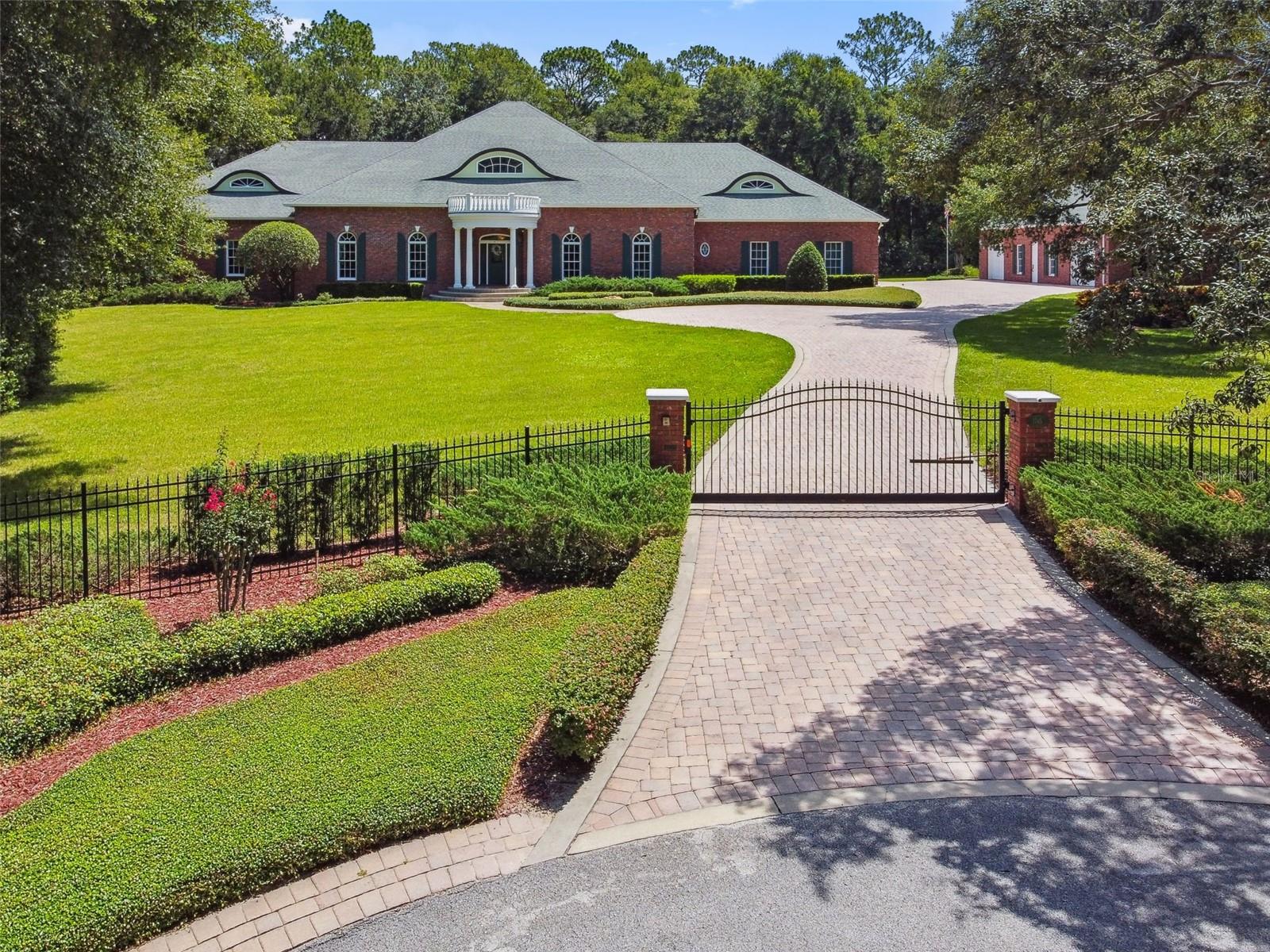 Welcome to a private luxury estate at the end of a peaceful cul-de-sac in the exclusive gated enclave of Taylor Woods. On 2.5 manicured acres, this custom-built masterpiece delivers a rare blend of timeless elegance, high-end craftsmanship, and everyday comfort. From the moment you arrive, the estate makes a grand impression with its stately paver driveway, white-pillared entry, and raised elevation, built on a solid concrete stem wall foundation with brick veneer for enduring quality. Inside, soaring ceilings, hardwood and tile floors, and more than a mile of crown molding set the tone for luxury living. Swarovski crystal chandeliers grace the foyer and formal dining room, which comfortably seats twelve and features a gas fireplace surrounded by black marble. The chef’s kitchen is designed to impress dual islands, solid wood cabinetry, a gas cooktop with downdraft, double ovens, a dedicated ice maker, and a butler’s pantry complete with prep sink, warming drawer, walk-in storage, and private entry to the dining room. The grand living room features custom built-ins, a gas fireplace and a one-of-a-kind original carousel horse centerpiece. Just beyond the grand living room and kitchen, a long and elegant hallway leads to the garden room—an inviting space for informal dining with floor-to-ceiling windows and a vaulted ceiling custom-painted with a serene sky and cloud motif. Continuing through the home, a wide gallery hallway—accented by graceful archways, sconce lighting and hidden hardwood flooring—leads to multiple bedrooms, including a flexible study with a tin inlay tray ceiling and an oversized office with ample storage, and even a convenient half bath with lanai access. The primary suite is a sanctuary featuring French door access to the lanai, two walk-in closets, a gas fireplace with marble surround, and an expansive en-suite bath with dual vanities, dual water closets and dual walk-in showers The laundry room is thoughtfully appointed with a sink, folding station and a hidden laundry chute connecting directly to the primary suite. Upstairs, the guest suite offers two bedrooms, a flex room, a full bath, and a comfortable sitting area with its kitchenette. The walk-in attic is directly accessible from this level with built-in shelving, lighting, and a 400-pound capacity electric lift that connects to the three-car garage below, making it effortless to move stored items between levels. The large lanai is partially under roof and is designed with entertaining in mind. Three sets of French doors and a separate entry door provide seamless flow to key areas of the home. Across from the lanai, the custom-designed dog park is an exceptional feature for pet lovers—partially covered and fully enclosed with fencing and premium artificial turf. The detached carriage house adds another 1,157 square feet, including a climate-controlled museum space and a fully equipped workshop with a car lift. Additional highlights include a steel-door safe room with air conditioning, a 20-kilowatt propane generator, impact-resistant Anderson windows and doors, full irrigation system with private well, and spray-foam attic insulation for year-round energy efficiency. This one-of-a-kind estate offers complete privacy while being just minutes from historic downtown DeLand, named “Best Main Street in America,” and within easy reach of beaches, major highways, shopping, restaurants, cultural events and top-rated schools.