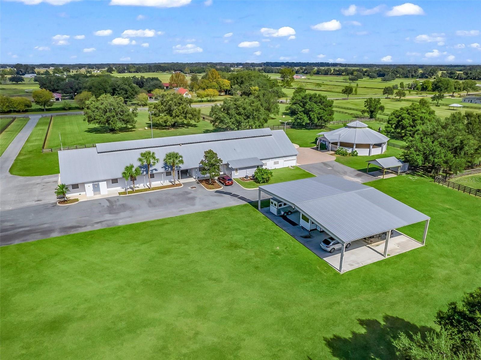 Located just 20 minutes from the World Equestrian Center, and 15 minutes from downtown Ocala, this expansive, fully fenced 20+ acre property offers the perfect blend of convenience and luxury for both equestrian enthusiasts and those seeking serene country living. The barn on the property is designed with optimal airflow in mind, featuring high-ventilated ceilings with skylights and a fan system to ensure a comfortable environment for you and your horses. Inside, you'll find 14 spacious stalls, each outfitted with automatic waterers and a one-piece matting system for ease of maintenance. Additional barn amenities include a feed room, storage area, an indoor wash rack, and a well-appointed tack area. For your guests or team, the barn also includes a guest air-conditioned half bath, along with a 2-bedroom, 1-bath apartment complete with a full kitchen, modern stainless-steel appliances, and ample living space. A rider’s lounge with a kitchenette and full bath provides an ideal retreat after a long day, while the air-conditioned tack/laundry room and office add even more functional space to this incredible facility. This property further elevates your equestrian experience with 10 paddocks with shelters, a 60-ft diameter enclosed round pen featuring a raised viewing area, and a 50×70 covered steel building with a concrete floor—perfect for a variety of uses. The meticulously maintained grounds include fully irrigated lawns and landscaping, complemented by large brick patio areas and stadium-quality lighting that ensures your outdoor activities can continue into the night. Additionally, 5 RV sites, a 40kW emergency generator that will power the entire farm, and a lightning protection system that adds peace of mind, while the prime location allows for quick access to the best of Ocala’s equestrian scene. This is more than just a property—it's a lifestyle, waiting for you to make it your own.