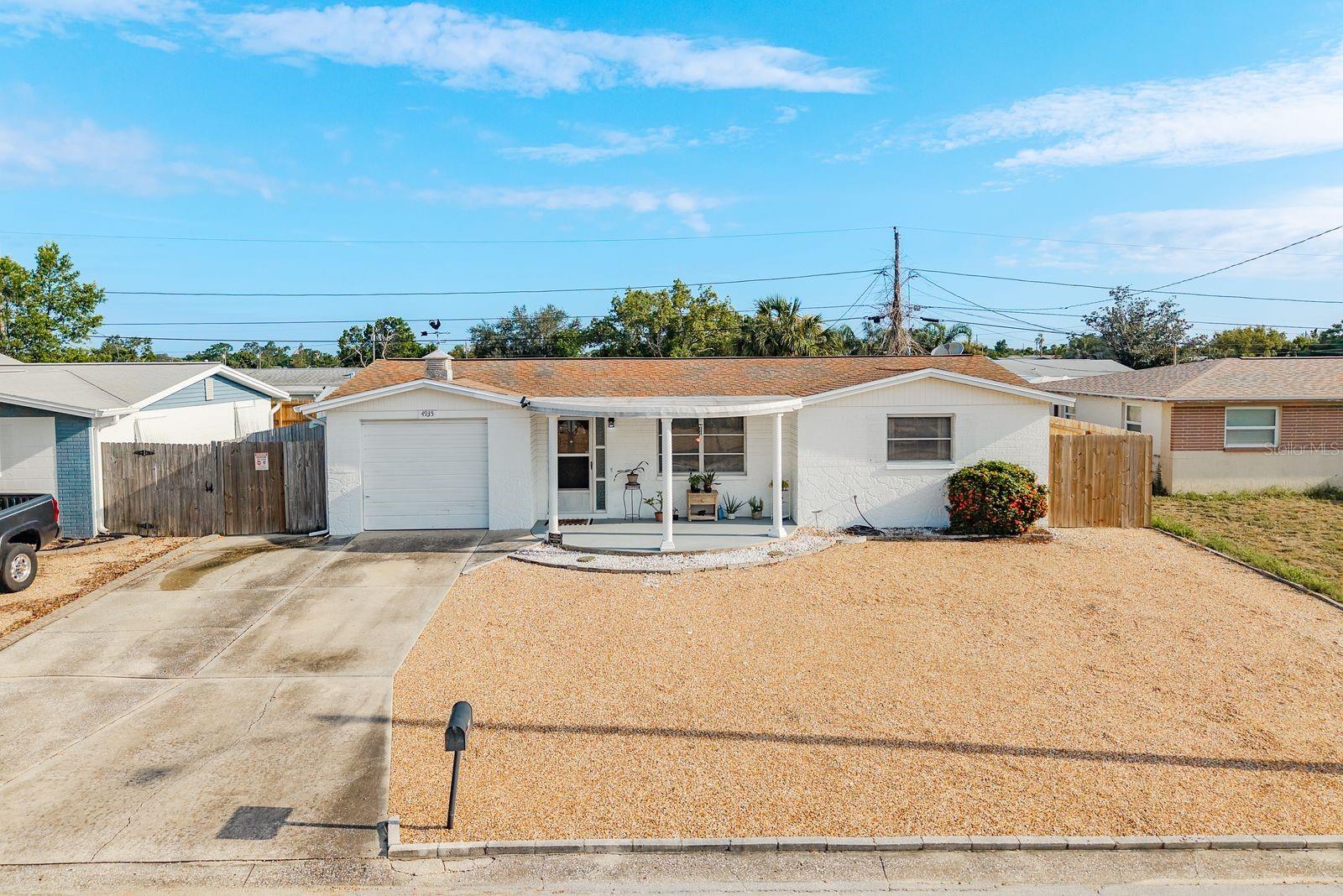 CHARMING & MOVE-IN READY! Step onto the spacious covered front patio and into a bright, open living area with easy-care terrazzo floors that flow throughout. The updated eat-in kitchen at the back of the home features stainless steel appliances, generous pantry space, and sliders leading out to a covered back patio—perfect for enjoying your morning coffee.
Both bedrooms share a full bath with a tub/shower combo, and a second bath with walk-in shower is located in the garage. The garage itself has been finished with a wall-mounted A/C unit, offering flexibility as a bonus space while still accommodating one car. Throughout the home you’ll find brand-new ceiling fans with LED lighting, window treatments, and a keyless entry Smart-lock adding comfort, style and convenience.
The property also features a two-car driveway, low-maintenance front landscaping, and a backyard with plenty of potential for sod or gardening. Located in a high-and-dry area just inside the Pasco County line, this home is close to shopping and daily conveniences—all with no HOA restrictions.