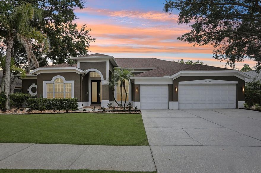 Tucked behind mature oaks on a quiet, tree-lined street in Odessa, 15720 Berea Drive offers a rare combination of refined craftsmanship and direct lakefront living on serene Lake Grace. Timeless curb appeal welcomes you home with warm taupe stucco, crisp white trim, a gabled archway entry framing 8-foot double doors, lush tropical landscaping, and a three-car garage tucked beneath a sweeping hip roof.

Inside, soaring 12-foot ceilings, layered crown molding, 8-inch decorative baseboards, and 24-inch porcelain tile run through every main living area, while plantation shutters dress the road-facing windows. The thoughtful floor plan flows effortlessly between formal and casual spaces, beginning with a combined formal living and dining room - anchored by decorative columns and a slider that frames the lake from the moment you arrive. A dedicated office sits at the front of the home, ideal as a study, library, or flex room.

The heart of the home is a beautifully scaled with an over-sized kitchen designed for serious cooking and lively gatherings. Crisp white raised-panel cabinetry rises to 42 inches and is capped with crown molding, granite counters with rich golden movement wrap the perimeter, and a striking deep-navy center island adds personality and prep space. Stainless KitchenAid appliances, a closet pantry, and a layered tray ceiling with pendant lighting complete the space, with lake views from the sink. The kitchen opens to a 17x22 great room framed by pocket sliding glass doors that disappear into the wall, blending interior and exterior into one expansive entertaining space.

The owner's retreat is a true escape, with hardwood flooring, lake and pool views, and two oversized walk-in closets featuring custom built-ins, a built-in jewelry safe, and a larger safe for important documents and family heirlooms. The renovated spa-quality primary bath features espresso shaker cabinets with abundant storage, exotic granite tops, illuminated LED vanity mirrors, and a frameless walk-in shower with a rain head, handheld wand, and full body-spray system. Three additional main-floor bedrooms include one with lake views and an en-suite that doubles as a convenient pool bath, while a generous 14x15 upstairs suite with private bath and walk-in closet works equally well as a fifth bedroom or bonus room. The interior laundry features 42-inch cabinets and a Bosch washer and dryer that convey with the home.

Outdoor living is where this home truly shines. A panoramic screen enclosure rises over a sun-drenched travertine deck framing a sparkling PebbleTec pool and raised spa with hand-laid blue mosaic tile. The expansive covered lanai feels like a true outdoor room, with a stunning stained tongue-and-groove wood ceiling, industrial-cage fans, recessed lighting, and a fully equipped outdoor kitchen featuring stacked stone, granite tops, a Fire Magic grill, beverage fridge, and Big Green Egg. Beyond the screen, the lot steps down to the shoreline of Lake Grace, surrounded by mature trees for a private, park-like setting. Easy access to the Veterans Expressway, top-rated schools, shopping, dining, and Tampa International Airport make this lakefront retreat as practical as it is beautiful.