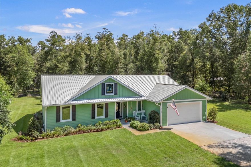 Within the peaceful community of Chesborough’s Corner in High Springs, this thoughtfully crafted home on 5 acres embodies quality, intention, and timeless appeal. Beyond the gracefully curved, tree-lined drive, this custom-built 2021 modern farmhouse is anchored by a pristine lawn that gives way to a backdrop of towering pines and oaks. Before heading inside, you will want to pause on the welcoming front porch, a perfect spot for morning coffee while taking in the quiet beauty of the natural surroundings. As you step through the front door, you are greeted by an expansive open-concept layout defined by high ceilings and luxury vinyl plank flooring that radiates natural light across the heart of the home. Overlooking the spacious living and dining areas is the chef-inspired gourmet kitchen, a perfect hub for entertaining with sleek quartz countertops, stainless steel appliances, a pantry with ample shelving, and a large central island. From casual gatherings to large celebrations, the living space’s intuitive design keeps everyone connected without interrupting the conversation. Glass doors off the dining area open to a lovely sunroom featuring a convenient half-bath and entry to the 2-car garage. Tucked away for maximum privacy, the primary suite serves as a true retreat and boasts a walk-in closet and ensuite with double vanities, a walk-in shower, and a linen closet. Two guest bedrooms and a full guest bath with a tub and shower combo provide ample space for friends and family members. Step outside to find a beautiful backyard featuring a patio and a detached 24x40 metal barn with a lean-to, roll-up door, electric, and water, making it the perfect workshop and garage for equipment and outdoor toys. With no HOA and 5 acres of versatile land, this property is also a haven for animal lovers, as both horses and chickens are welcome. Beyond the aesthetic, this home is engineered for modern efficiency, featuring energy-saving spray foam insulation in the attic, irrigation around the home, a stem wall foundation, a lifetime warranty on windows, underground utilities, and high-speed Wi-Fi capability. Located in Chesborough’s Corner, you are just minutes from the world-famous freshwater springs and the Santa Fe River, while enjoying a convenient commute to I-75 and the city amenities of Gainesville. Rarely does a property capture the quiet soul of the Florida countryside while offering the luxurious comforts of a custom-built retreat, but this property does exactly that. Schedule a private tour today to experience this High Springs gem for yourself!