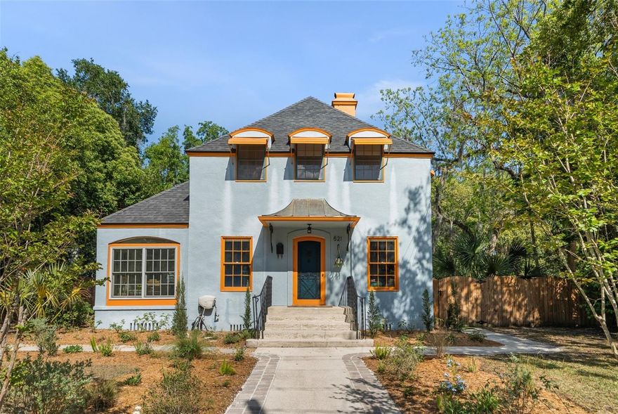 A rare offering in the heart of Duckpond, this early 1900s home blends classical architecture with intentional moments of whimsy, creating a home that feels both grounded in history and playfully alive.  Framed by a bespoke wooden archway and surrounded by intentional landscaping, 521 NE 6th Street is as much an experience as it is a home.
With roots tracing back to the early 1900s, and possibly earlier, this property carries a story few homes can offer. Once associated with prominent Gainesville families, including Abraham Pepper, it has long been a place of gathering, conversation, and community. From its early days on what was once N. Franklin Street to today, its legacy continues in both its presence and preservation.
Step through the front door, and you’re immediately drawn into a warm, inviting living space anchored by the original limestone and marble fireplace. From here, your eye travels effortlessly through the dining room, into the kitchen, and out to the back patio beyond, a layout that feels both open and intentional. 
To your left, a striking blue staircase introduces a bold moment of contrast, while just beyond, a light-filled sunroom offers a peaceful retreat.
The dining room is accented with custom built-ins that feel as though they’ve always belonged. Nearby, a tucked-away flex space, currently a playroom, offers versatility and could just as easily be an office or reading nook. This space also provides access to a conveniently placed downstairs bathroom, ideal for both daily living and guests.
The standout kitchen is a designer’s dream. Reform oak cabinetry, Müller Van Severen HDPE countertops, and checkered cement tile create a palette that feels both grounded and modern. A suite of Fisher & Paykel appliances, including an induction range and integrated dishwasher, is seamlessly woven into the design.
Whimsical moments appear in all the right places, with thoughtfully chosen colors and finishes that create statement pieces without overwhelming the space, adding personality and depth to the home’s overall design.
Upstairs, three bedrooms and a bath sit beneath softly angled ceilings, where dormer windows bring in light at unexpected angles. Built-in bookcases add both detail and function, while one room offers attic access, extending the home’s sense of possibility.
Throughout, the finishes feel quiet but deliberate, like skim-coated walls, fresh interior paint, and refinished floors (2023), paired with a curated selection of lighting from Gubi, HAY, Raw Color, and Dioscuri, along with trimless recessed fixtures that allow the architecture to remain the focus. Microcement in the bathroom and sunroom adds a soft, tactile contrast to the home’s historic bones.
Step outside, and the home continues to reveal itself in layers. The yard unfolds as a series of spaces to gather, to garden, to linger. Arborvitae and birds of paradise will grow into a lush, natural enclosure over time, offering both privacy and presence. At the rear, a garage/workshop with an additional enclosed space invites possibility for a studio, workspace, or future ADU. A shared drive provides access without interrupting the experience.
Homes like this are rarely available, where history, design, and livability come together so seamlessly. Schedule your private showing and experience 521 NE 6th Street for yourself.