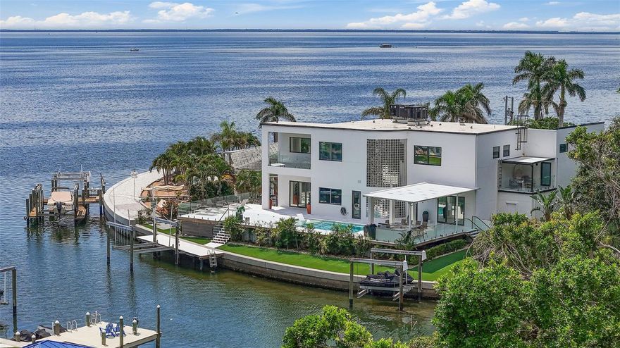 Where modern luxury meets effortless waterfront living, this exceptional St. Petersburg estate offers 180 feet of deep-water frontage, expansive water views, and direct boating access to Tampa Bay and the Gulf. Completely renovated in 2022, this 4-bedroom, 4-bath smart home with a 3-car garage is constructed with concrete block and metal framing—no wood—and is elevated for added peace of mind. Offered fully furnished, this home is truly move-in ready.  Exterior upgrades include a standing seam metal roof, impact-rated windows and doors with a custom front entry, smooth stucco finish, and glass railings surrounding the pool for unobstructed views. Inside, the open-concept layout is highlighted by high ceilings, marble flooring, and a designer kitchen featuring leathered stone countertops, inset cabinetry, hidden appliances, ice maker, and a dry bar with wine refrigeration. Smart home features provide control of lighting.  All four oversized bedrooms offer water views, custom closets, and en-suite baths with high-end finishes, including rain showers and modern fixtures. The primary suite features an electric fireplace, dual custom walk-in closets, and a private balcony with sweeping open water views. The spa-style primary bath includes dual floating vanities, a soaking tub, dual rain showers, and custom tilework. Additional features include a fully finished, air-conditioned 3-car garage with epoxy flooring and recessed lighting, plus a versatile loft space above the garage ideal for an office, gym, or guest suite, complete with its own balcony and water views. Updated HVAC systems include rooftop units, new ductwork, slot diffusers, and multiple mini-splits for efficiency.  Outdoor living is designed for entertaining, with a heated saltwater pool featuring fountains, non-slip pavers, glass railings, and professionally designed low-maintenance landscaping with LED lighting. The covered lanai includes a full outdoor kitchen, while additional spaces offer a gas and wood-burning fire pit and turf recreation areas.  The updated dock system features a 20,000 lb boat lift, dual personal watercraft lifts, composite decking, water and electric service, integrated storage, and dual lighted stair access.  Conveniently located approximately 3 miles from downtown St. Petersburg, 7 miles from St. Pete Beach, and 22 miles from Tampa International Airport. Flood insurance is currently approximately $800/year due to elevation and may be assumable. Seller may consider owner financing with 20% down.
