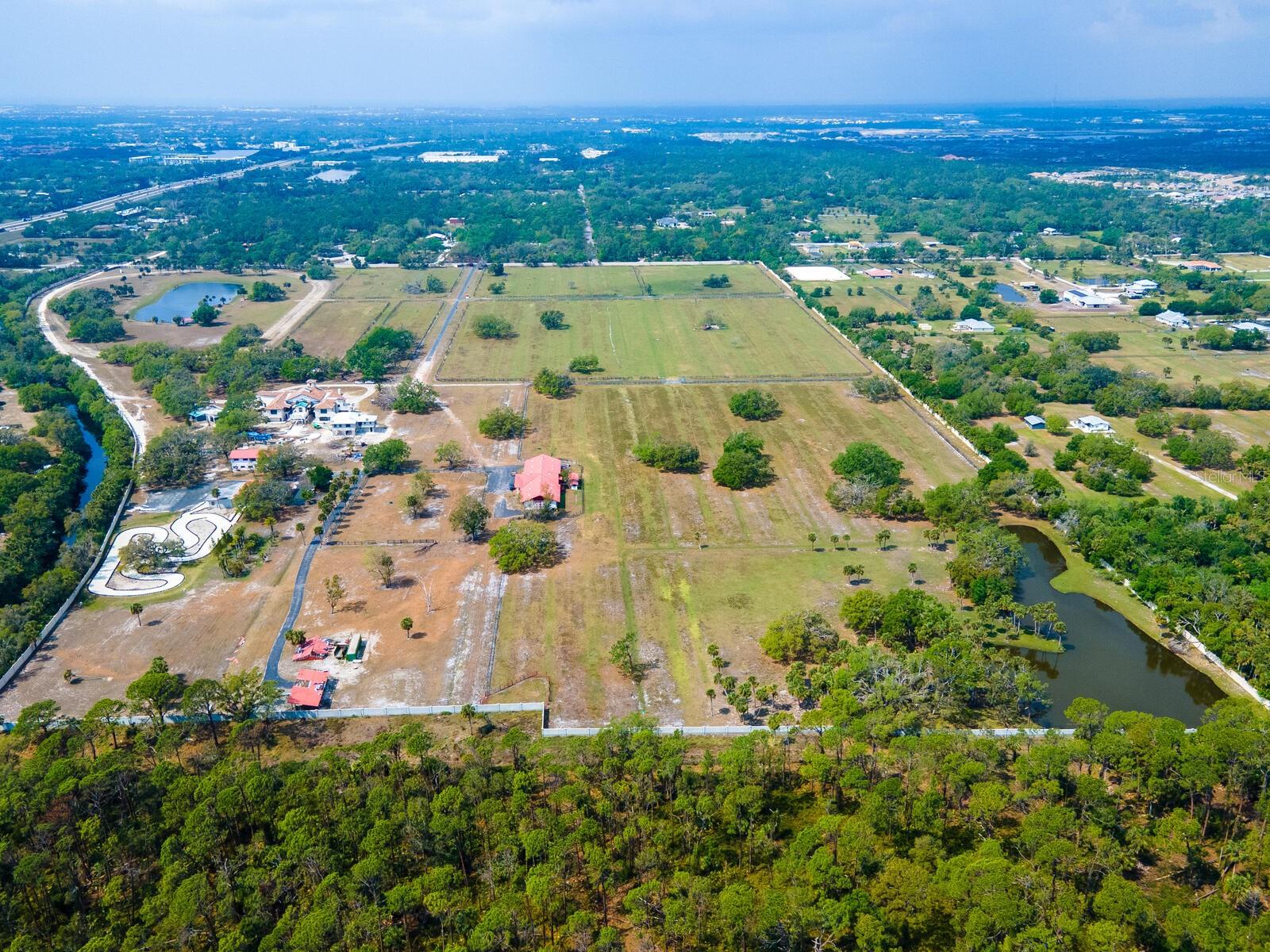 Under Construction. Set on approximately 102 acres just eight miles from world-class Gulf beaches, this extraordinary ranch estate presents a rare opportunity to complete a one-of-a-kind residential compound in Venice, Florida. The non-completed main residence spans more than 24,500 total square feet, with 18,869 square feet of interior space, including seven bedrooms, seven full baths and six half baths. The estate is framed and plumbed, ready for drywall, offering its next owner the opportunity to fully customize the final phases of construction. The seller’s plans reflect a primary suite including multiple sitting rooms, dual walk-in closets, and a spa-style bath with walk-in showers. A chef’s kitchen is designed to accommodate two bar areas, a full dining room and a commercial-grade freezer with a walk-in pantry. A grand living room is highlighted by skylights, while plans include guest suites, formal living rooms, library/office overlooking the amazing pool area, private theatre, gym and dual laundry rooms. The estate also features a poolside casita guest house with two separate living dwellings, one a three-bedroom, two-bath, the other a one-bedroom, one-bath to be completed by the buyer. Outdoor living is centered around a designed 100,000-gallon geothermal-heated pool, complete with walk-in entry, water slides, lounging areas, outdoor kitchen, covered pavilion, and poolside baths and showers. Equestrian enthusiasts will appreciate the 21-stall barn with a community room, kitchen, full bath and two self-contained apartments. Multiple detached garages accommodate more than 10 vehicles and provide additional storage. A full stone perimeter wall surrounds the estate, ensuring privacy and security. With potential to subdivide or maintain as a legacy family compound, this generational opportunity offers architectural scale, acreage and vision unlike anything else in the region.