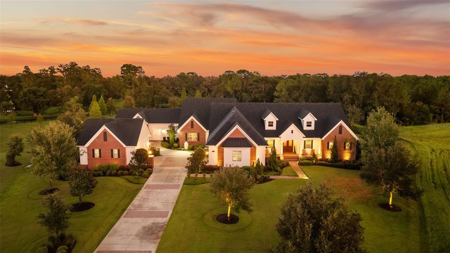 Discover timeless Southern charm and modern luxury in this single-story brick estate located in the prestigious guard-gated community of Stonelake Ranch. Built in 2017 on a private cul-de-sac, this home rests on a sprawling 2.53-acre parcel, set 50 feet above sea level with a desirable northwest-facing orientation. Offering nearly 5,900 sq. ft. of living space (8,890 sq. ft. total) with 5 bedrooms and 5 bathrooms, the residence blends elegance, comfort, and functionality. Inside, hardwood floors, crown molding, and thoughtful details define the living spaces. The gourmet kitchen features a large island with pendant lighting and seating for four, a farmhouse-style undermount sink, walk-in pantry, and a complete KitchenAid appliance package including a five-burner gas cooktop with pot filler and double ovens. Formal areas include a sitting room with three built-in desks currently used as a piano room, a private office with an exposed brick wall, and a dining room with a dramatic chandelier. The primary suite is a retreat with exposed beams, dual walk-in closets, and a spa-inspired bath featuring a clawfoot soaking tub, oversized walk-in shower with multiple shower heads, makeup vanity, and linen closet. The family room offers a gas fireplace, custom built-ins, surround sound, and triple pocket, sliding glass doors leading to the pool deck. Designed for entertaining, the home features a spacious bonus room with a wood-beamed ceiling, wet bar with wine fridge and icemaker, surround sound, and quadruple pocket sliders opening to the outdoors. A theater room and an indoor fitness center complete the lifestyle amenities. Outdoor living includes a sparkling pool and spa, outdoor fireplace, summer kitchen, and expansive paver deck with ample seating. Car enthusiasts will appreciate the garages: a climate-controlled three-car with two lifts (room for five vehicles), a secondary two-car with built-in cabinetry, plus a detached two-car. A basketball court, extended parking pad, and impressive driveway complete the property. Stonelake Ranch offers 680 acres of rolling landscape along Lake Thonotosassa, the county’s largest lake at 880 acres. Community amenities include a lakeside lodge and fitness center, private boat launch and storage, tennis and pickleball courts, playground, equestrian trails, and a 100-acre preserve. Ideally located just 20 minutes from Downtown Tampa, the estate is convenient to Tampa International Airport, Lakeland Regional, Tampa General, Moffitt Cancer Center, and the VA Hospital, with Clearwater Beach only a short drive away. A rare opportunity to own a private estate that blends elevation, orientation, and elegance with Florida luxury.