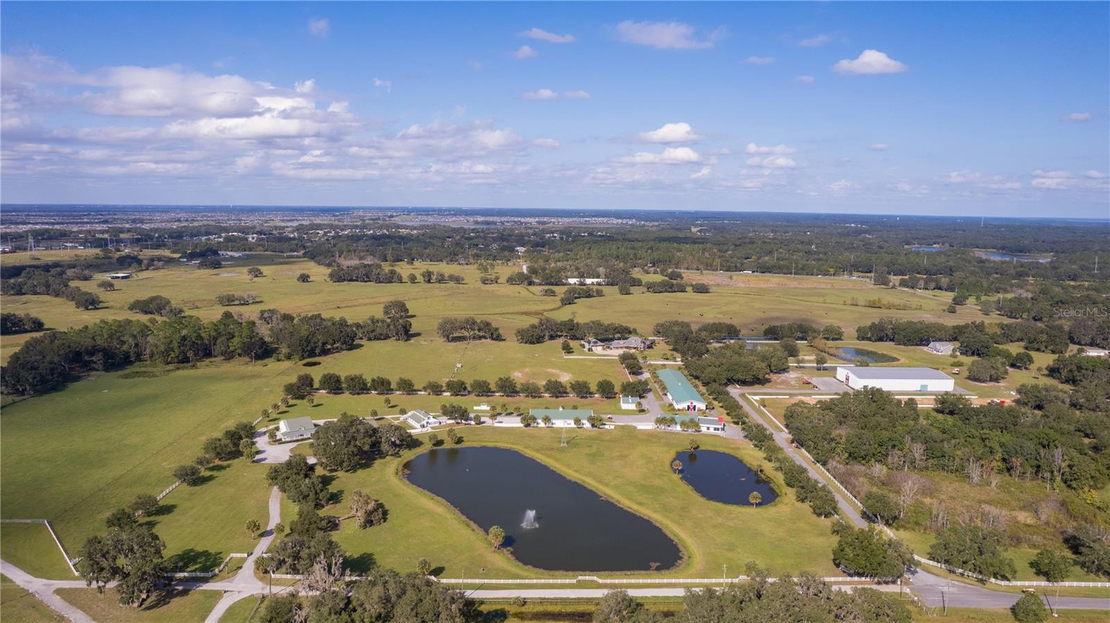 Introducing an Extraordinary 16+ Acre Estate Home: A harmonious blend of upscale living and serene country charm awaits you just a few miles from the vibrant cities of Leesburg, Mount Dora, Clermont, The Villages and only an hour or so to both Orlando or Tampa. This exclusive property boasts over 30,000 square feet under roof, making it a rare gem in the real estate landscape.
As you enter through the gated and fenced property, you'll be greeted by large winding driveways leading around water features adorned with elegant fountains. The landscape evokes the grandeur of Southfork Ranch, reminiscent of the iconic television show "Dallas." The main home, spanning over 4400 square feet, offers climate-controlled living spaces and features over 2100 square feet of wrap-around porches and lanais.
Upon reaching the entrance, one is compelled to pause, sipping sweet tea or lemonade in rocking chairs while taking in the panoramic views of nature and wildlife. The main living room impresses with soaring ceilings, a floor-to-ceiling fireplace, and sliding glass doors that seamlessly bring in the beauty of the surrounding countryside.
This remarkable property is designed for both entertaining and practicality. The main home comprises 5 full bedrooms and 4 bathrooms, including a spacious 675+ square foot party room with a wrap-around bar. The detached 2000 square foot garage offers versatility, with a loft and space for an in-law suite, ranch hand apartment, or exercise room, complete with separate HVAC.
In addition to the main residence, a guest home spanning two stories and over 2000 square feet provides 3 bedrooms, 2 bathrooms, and 2 kitchens – ideal for long-term rental income or accommodating visiting friends and family.
The estate further includes several purpose-built structures, such as a 5160 square foot steel building (labeled show barn), a 1080 square foot tractor barn, and a substantial 12,500 square foot insulated steel building. For those with a penchant for automotive collections, there's ample space for storage in buildings equipped with bathrooms and large roll-up doors.
Whether you envision hosting events, embracing the tranquility of country living, or enjoying the expansive wildlife, this exclusive property offers a unique blend of elegance, peace, and your very own slice of paradise. Don't miss the opportunity to make this exceptional estate your home.