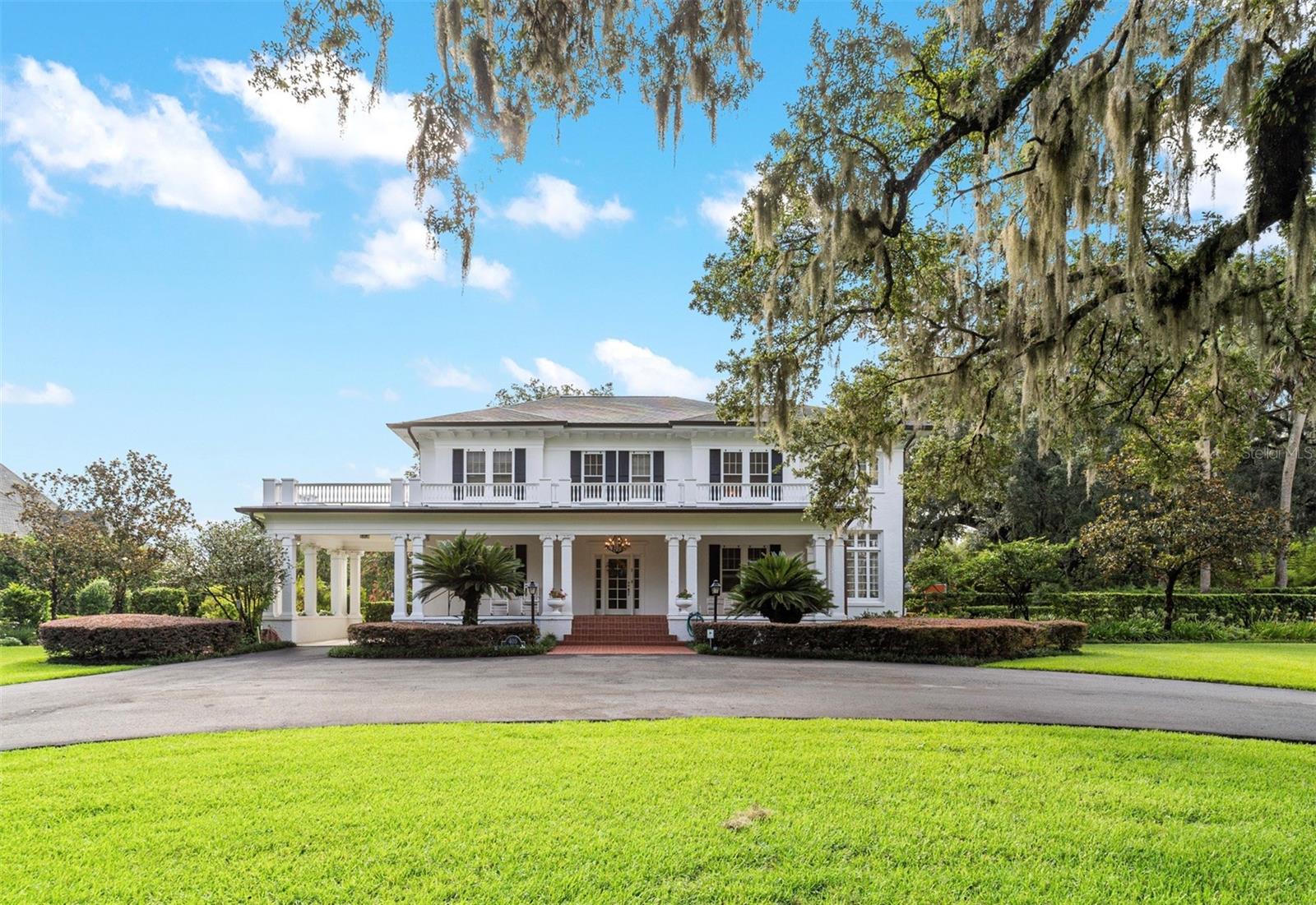 Welcome to this elegant and meticulously kept historic Ocala estate, with timeless character and 2.46 acres of beautifully landscaped grounds. Situated among antique roses, a perennial garden, and majestic oaks, this stately 5-bedroom, 3.5-bath residence welcomes you with a beautiful front porch, offering just one of the perfect spots to enjoy the peaceful surroundings. Step inside to discover several living spaces including formal dining room, living room with fireplace and sunroom attached. Another cozy sitting room with fireplace, leads to outdoor patio and deck. Five charming sunrooms fill the home with natural light. The custom kitchen features rich cherry and maple cabinetry, granite countertops, a built-in refrigerator, gas dual-fuel range, wall oven and microwave, plus a charming breakfast room and mudroom. Just off kitchen is a small built-in office space. Downstairs bedroom, with sunroom attached, has updated bath with walk-in shower and soaking tub. A wooden staircase leads to second story with upstairs landing perfect for relaxing. The primary bedroom, with built-in shelving and 2 master closets, has its own sunroom and updated master bath with wainscoting, double vanity and large walk-in shower. (5th bedroom is located adjacent to primary suite and could second as a study, sitting room or nursery. Attached sunroom is currently being used as a large closet). The other 2 upstairs guest rooms share an updated Jack and Jill bath, with one bedroom having a sunroom attached and the other features a large walk-in closet and built-in cabinets. All baths throughout home have been fully redone with tumbled Italian marble and updated fixtures. Authentic details throughout the home, include 9-10 ft ceilings, terracotta tile and stucco over concrete construction, plaster walls in excellent condition and oak and heart of pine flooring. Home also has extensive storage, including several walk-in closets (plus a cedar closet) and basement with access from inside or out. A special feature of this home is the massive cedar lined and temperature controlled 12x19 wine room, located off garage, with travertine floors, private patio entrance and capacity for approx. 2,300 bottles—perfect for collecting and entertaining. A newly resurfaced saltwater pool, which is fully fenced, is located steps from back patio and deck, and has access to half bath close by. This home is complemented by expansive covered porches, mature landscaping and the warmth of natural materials throughout. This quiet in town location is just outside the historic boundaries and is located on a corner lot with entrances from 3 streets. Take advantage of this rare opportunity to own a piece of Ocala’s history—which has been lovingly maintained and is move-in ready.