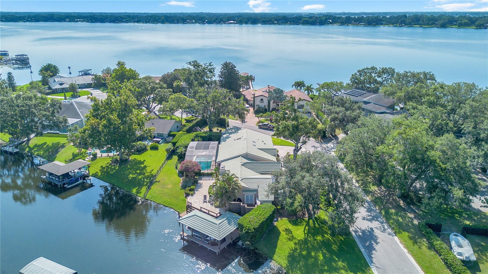 Set on the corner of a quiet cul-de-sac on the Conway Chain of Lakes, this lakefront estate strikes the rare balance between legacy architecture and modern function — with a dock, pool, and layout built to elevate everyday living. With 4 bedrooms, 3 full bathrooms, an office, and over 4,000 square feet under air, it lives large without feeling overbuilt — grounded by clean lines, custom finishes, and unobstructed water views from almost every angle. From the street, the home’s presence is understated but confident. A wide paver driveway, manicured landscaping, and custom hurricane shutters frame the entry, while dual garages and mature oaks provide privacy and timeless curb appeal. Inside, the foyer opens to a formal dining space and sunlit living room anchored by a wood-burning fireplace. Large nearly floor to ceiling windows, draw you straight toward the screened-in pool deck and lake beyond — where covered seating, outdoor fans, and a pool fence offer year-round comfort and security. The kitchen was designed with both daily rhythm and entertainment in mind — featuring a long prep peninsula, wine fridge, and seamless views of the water. Speakers are wired throughout the home (and outdoors) for easy ambiance, and the lake-fed irrigation system means the grounds stay lush with zero water bill. The split floor plan offers true flexibility. Tucked on one side of the home is a spacious primary wing with double-door entry, sitting area, and two custom walk-in closets. The ensuite bath is oversized and window-lined, with dual vanities, soaking tub, and separate shower. On the opposite side of the home are four additional bedrooms, including two with their own private bathrooms — ideal for guests, multigenerational living, or live-in support. An office with built-ins, a large laundry room with utility sink, and extensive hallway closets round out the interior functionality. Out back is where this home fully delivers. The new Cichra-built dock features a covered 7,500 lb boat lift and wraparound walkways — shaded by a custom tile roof with lighting and ceiling fan already in place. The bay opens directly to Little Lake Conway, one of Central Florida’s premier private-access ski lakes. Whether you're cruising to lunch, catching sunset from the dock, or hosting poolside — this backyard was designed for connection. Major systems have been thoughtfully upgraded: whole-house Generac generator with a 500-gallon buried propane tank (gas remaining negotiable), tankless gas water heater, full home replumb, Armstrong-installed Emtek bump locks, wired security cameras, and an upgraded ADT system. There’s also a storage shed tucked away for convenience. Located in a private, no-HOA enclave with tree-lined streets and custom homes, 525 Mandalay Rd offers lakefront living without compromise — where function, flow, and location meet on your terms.
