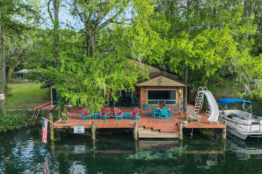 Experience classic Florida magic tucked along the legendary Rainbow River — and yes, you just might want to stay forever.
Built in 1953, this warm and soulful riverfront home offers 2 bedrooms and 1.5 bathrooms in the main house, plus an additional bedroom and bathroom in the detached guesthouse. Cedar walls throughout give the home its signature cabin-cool, river-relaxed character — the kind of place that slows your heartbeat the moment you walk in. Tile floors keep things easy and comfortable, while the cozy kitchen features granite countertops and recently updated appliances.  Each bedroom tells its own story: one looks out over the garden, the other opens to the river. Wake up to morning fog rolling softly over the water, herons gliding through the mist, and turtles perching on sun-warmed driftwood as the day gently stirs to life. The massive waterfront deck is just steps from your bedroom door — grab a book, a journal, or a cup of coffee and settle into one of the Adirondack chairs. Breakfast tastes better here.  Rainy Summer Day, no worries, the enclosed oversized lanai overlooks the river - curl up, chill out, and just take in the scenery.  Rain or shine, time moves more slowly here. That's the point.  But we are in Florida, where endless summer days warm up, and the real fun begins.  A waterfront slide, rafting, boating, kayaking, and the pure wonder of the Rainbow River await. After a full day of adventure, rinse off at the outdoor shower or use the convenient exterior entrance directly to the bathroom and bedrooms. This home is also actively generating rental income and is available turn-key — details provided upon request.
The detached guesthouse is a wonderful bonus, offering a comfortable living space with a Murphy bed, a private bedroom, a recently remodeled bathroom, and a lovely lanai overlooking the fire pit — perfect for family, guests, or additional income potential. Round it all out with an oversized 2-car detached garage for all the gear, toys, and storage you need.
Peace of mind comes included: roof replaced in 2020, HVAC and hot water heater both new in 2025, and a soft water system already in place. This home has been loved by every generation that has called it their own, and that sense of warmth and care is felt in every corner.
Perfectly situated just minutes from Downtown Dunnellon, Blue Run Park, and Rainbow Springs State Park, with easy access to Crystal River, Inverness, Hernando, and Ocala for those days when you're ready for a change of scenery — though once you're here, that urge may be hard to find.  This is a rare opportunity to own a place where the river lifestyle is the amenity, and where leaving is the hardest part.