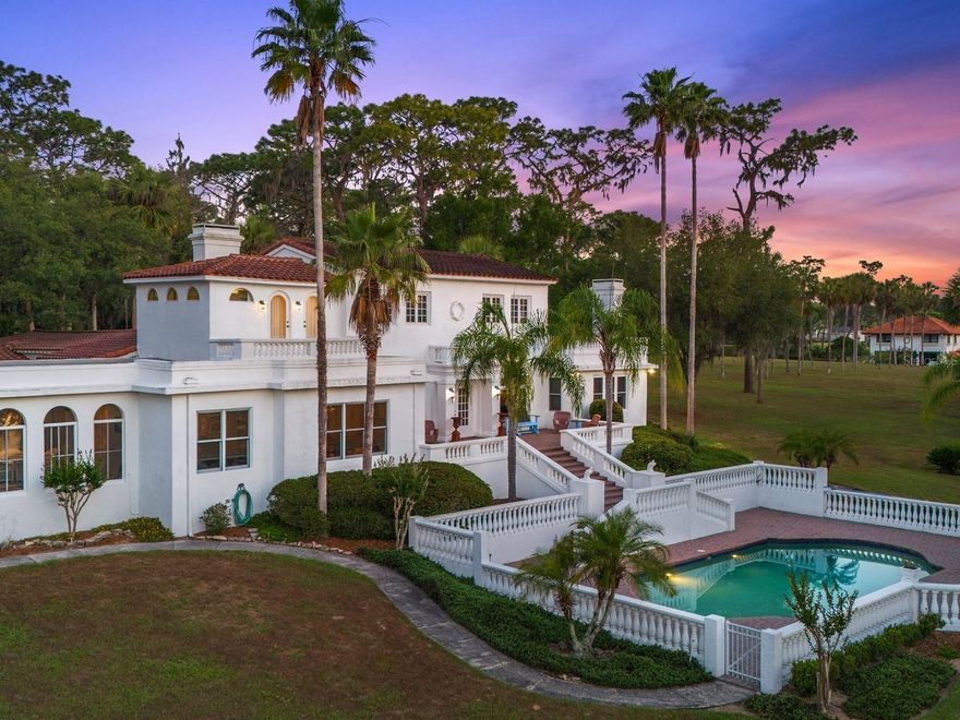 Come, step back into time to a magnificent waterfront Mediterranean estate that is perfectly positioned on 6 acres and 442 feet of direct frontage on pristine spring fed Lake Dalhousie where residents enjoy swimming, fishing, boating, water skiing and kayaking. A true retreat from the city life and one of the prettiest areas in Lake County. It enjoys the best of both worlds, uncrowded, peaceful country living, but close to shopping, major highways and the beaches. The grounds are enchanting but become sublime as you take in the spectacular early morning sunrise and golden hour that reflects on the home in a rich fairy tale glow. Stroll through the grounds where you will find stately grandfather oaks, bricked walkways, 1926 domed pavilion and emerald lush gardens all irrigated from the lake. You will notice the original 4-story water tower which, is no longer in use but stands tall capturing attention, making it one of the homes most iconic features. Commissioned with grandeur and built to endure in 1926 by Dr. Edgar J. Banks, a noted archeologist who began coming to Eustis in 1916 and today, this spectacular Mediterranean is ready to celebrate her 100th year old birthday. A peaceful courtyard entry with a stately fountain, loggias and Mahogany glass door entry add to the excitement and hint at the elegance within. Approximately over 6,200 square feet of living area consist of 2 master suites, 4 guest bedrooms and 5 1/2 baths. Upgraded plumbing and electric, volume ceilings, graceful arches, beautiful oak wood flooring, ornate fireplaces, large baseboards, iconic chandeliers, original Tudor style windows and newer windows that include Pella, Andersen, Marvin and Jeld-Wen, blend period charm with newer and modern conveniences. The grand ballroom overlooks the lakefront and features large parquet flooring and cherry wood inlay. The volume ceilings are graced with beautiful chandeliers, decorative hand carved plaster border and showcased with a handsome Artisan European gas fireplace. French doors open wide to the outdoor terrace which overlooks the 20x40 inground pool with stone paver decking, and mesmerizing views of the lake. The formal dining room features parquet flooring, Tudor style windows, coffered ceilings and original gas fireplace with a white mantle that has been delicately carved with the words Dolce Far Niente, meaning Sweetness of Doing Nothing. The generous kitchen, breakfast room and family room overlook the lakefront and have been completely redesigned with oak flooring, Quartz countertops, stainless steel appliances, French Country cabinetry and marble backsplash. The exterior back of the home stands tall and magical and features a magnificent focal point, designed with an abundance of white balustrades, the 20x40 inground salt pool, a terrace that spans the back of the home and a private master suite second story balcony. Perfectly designed for grand scale entertaining or tent the lawn for a beautiful outdoor wedding. The back yard features a gentle slope to the lakefront with long extended dock and a boathouse that currently houses a 21-foot boat and room for another. The main house features a 2-car garage, and another 4-1/2 car garage was added to the 4-story water tower. Other highlights include a very clean and neat large basement with upscale Kinetico water system and other mechanicals. This is a rare opportunity to own an original and architecturally stunning Mediterranean period home that seldom comes to market.