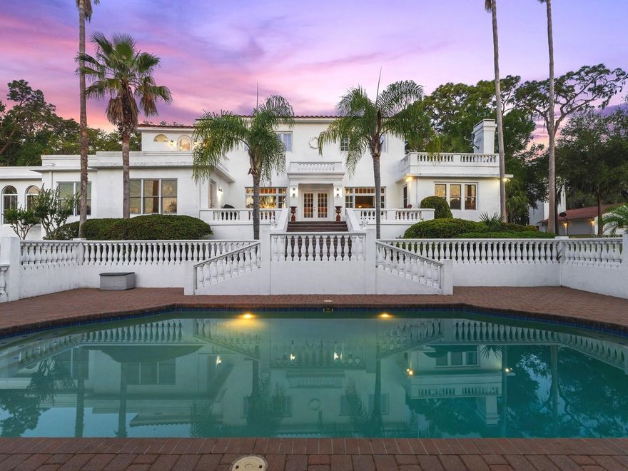 Come, step back into time to a magnificent waterfront Mediterranean estate that is perfectly positioned on 6 acres and 442 feet of direct frontage on pristine spring fed Lake Dalhousie where residents enjoy swimming, fishing, boating, water skiing and kayaking. A true retreat from the city life and one of the prettiest areas in Lake County. It enjoys the best of both worlds, uncrowded, peaceful country living, but close to shopping, major highways and the beaches. The grounds are enchanting but become sublime as you take in the spectacular early morning sunrise and golden hour that reflects on the home in a rich fairy tale glow. Stroll through the grounds where you will find stately grandfather oaks, bricked walkways, 1926 domed pavilion and emerald lush gardens all irrigated from the lake. You will notice the original 4-story water tower which, is no longer in use but stands tall capturing attention, making it one of the homes most iconic features. Commissioned with grandeur and built to endure in 1926 by Dr. Edgar J. Banks, a noted archeologist who began coming to Eustis in 1916 and today, this spectacular Mediterranean is ready to celebrate her 100th year old birthday. A peaceful courtyard entry with a stately fountain, loggias and Mahogany glass door entry add to the excitement and hint at the elegance within. Approximately over 6,200 square feet of living area consist of 2 master suites, 4 guest bedrooms and 5 1/2 baths. Upgraded plumbing and electric, volume ceilings, graceful arches, beautiful oak wood flooring, ornate fireplaces, large baseboards, iconic chandeliers, original Tudor style windows and newer windows that include Pella, Andersen, Marvin and Jeld-Wen, blend period charm with newer and modern conveniences. The grand ballroom overlooks the lakefront and features large parquet flooring and cherry wood inlay. The volume ceilings are graced with beautiful chandeliers, decorative hand carved plaster border and showcased with a handsome Artisan European gas fireplace. French doors open wide to the outdoor terrace which overlooks the 20x40 inground pool with stone paver decking, and mesmerizing views of the lake. The formal dining room features parquet flooring, Tudor style windows, coffered ceilings and original gas fireplace with a white mantle that has been delicately carved with the words Dolce Far Niente, meaning Sweetness of Doing Nothing. The generous kitchen, breakfast room and family room overlook the lakefront and have been completely redesigned with oak flooring, Quartz countertops, stainless steel appliances, French Country cabinetry and marble backsplash. The exterior back of the home stands tall and magical and features a magnificent focal point, designed with an abundance of white balustrades, the 20x40 inground salt pool, a terrace that spans the back of the home and a private master suite second story balcony. Perfectly designed for grand scale entertaining or tent the lawn for a beautiful outdoor wedding. The back yard features a gentle slope to the lakefront with long extended dock and a boathouse that currently houses a 21-foot boat and room for another. The main house features a 2-car garage, and another 4-1/2 car garage was added to the 4-story water tower. Other highlights include a very clean and neat large basement with upscale Kinetico water system and other mechanicals. This is a rare opportunity to own an original and architecturally stunning Mediterranean period home that seldom comes to market.