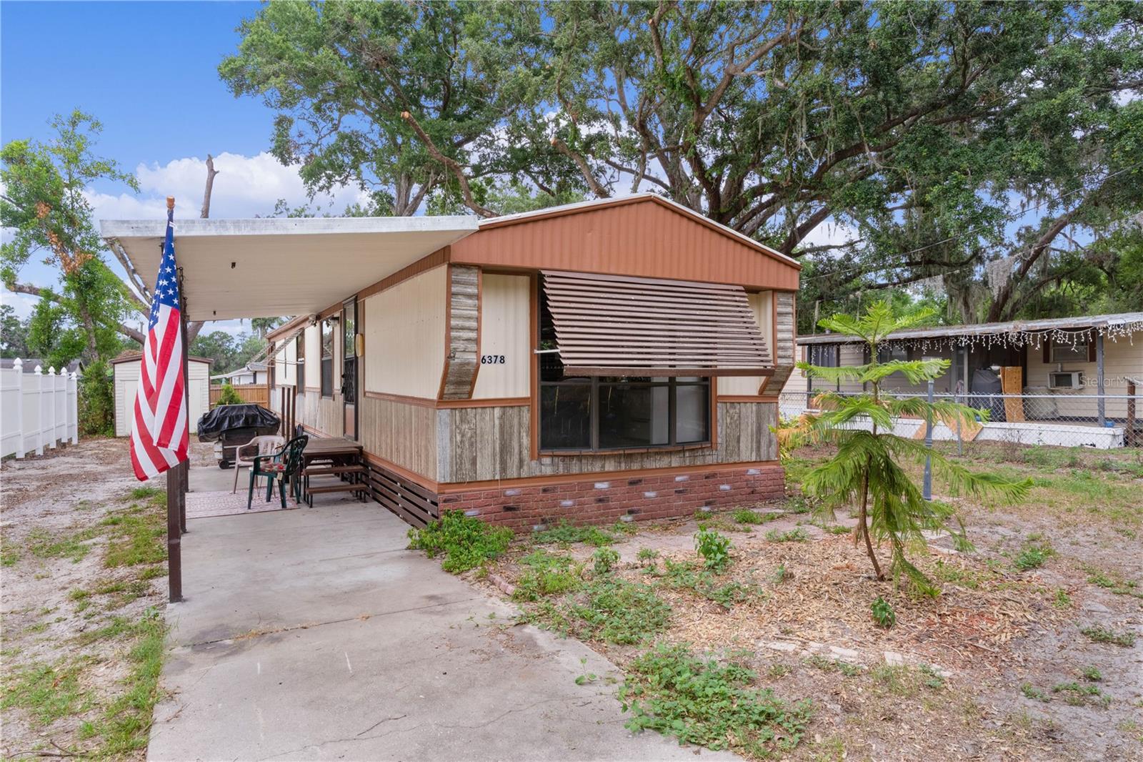 Welcome to this cozy, fully furnished and well-maintained single wide home with recent updates, perfectly situated on a fenced lot just minutes from The Villages®. There is NO lot rent for this home, making it an even more attractive opportunity for homeowners seeking affordability and freedom. This home offers a unique blend of comfort, convenience, and character. The exterior features durable metal siding, a matching metal roof, a carport and central A/C, complemented by decorative faux brick/stone skirting and protective awnings. Step inside to a spacious living area with vaulted ceilings and a ceiling fan, creating an open and airy feel. The eat-in kitchen includes a breakfast bar with overhead display storage, ideal for showcasing your favorite glassware. You’ll appreciate the wood cabinetry, double sink, and a lighted ceiling fan for added comfort. This home offers two nicely sized bedrooms, both with ceiling fans, and a shared full bath. An indoor laundry adds to the convenience. Enjoy your mornings in the enclosed lanai—perfect for sipping coffee, hosting game nights, or simply relaxing. The covered side porch provides ample space for a picnic table and grill, making it ideal for outdoor entertaining. Whether you're looking for a full-time residence or a winter retreat, this charming home is a must-see! Recent updates to this home include: vinyl fence, new A/C fan and capacitor, new well with water lines, motor and pressure regulator, new shut off valves and faucets. In addition to the home is an approximately 200 square foot shed included.